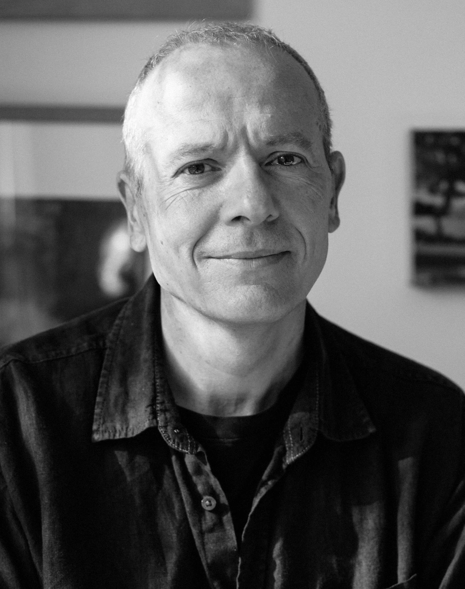 Black and white portrait of a person with short hair wearing a dark button-up shirt, smiling slightly, and looking at the camera.