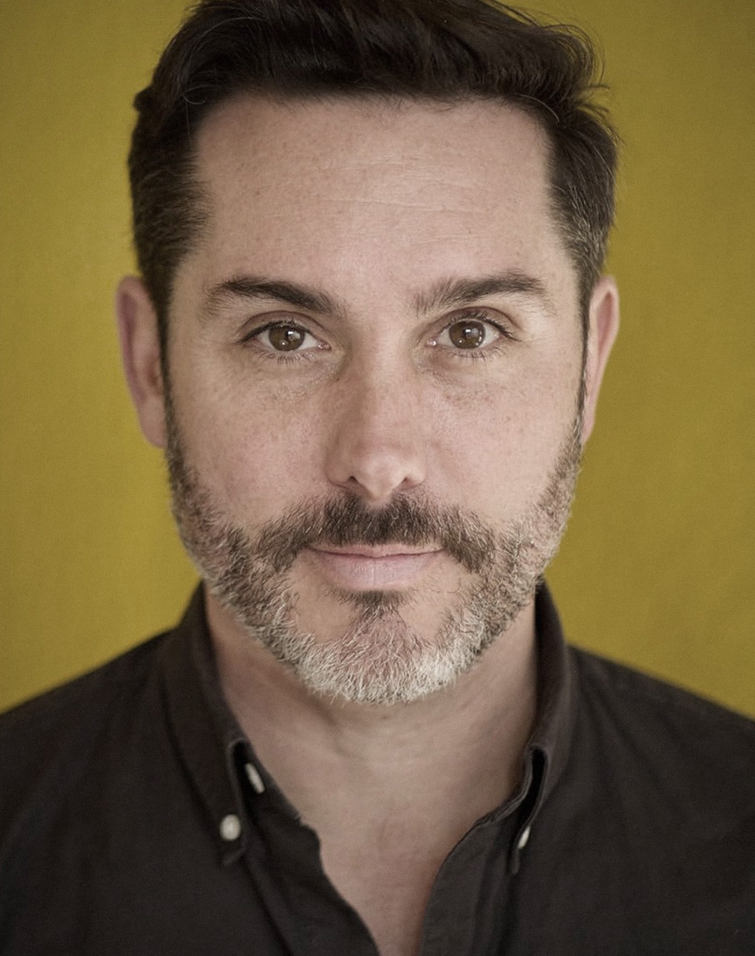 Man with short hair and beard against yellow background.
