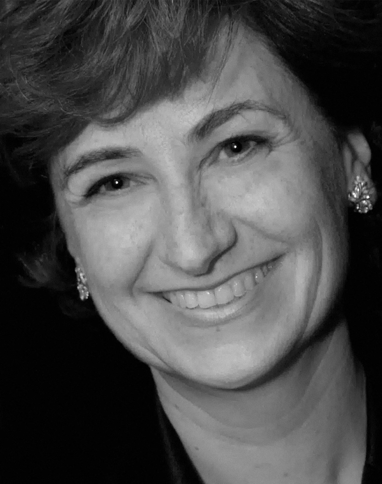 Black and white portrait of a woman smiling, wearing earrings.