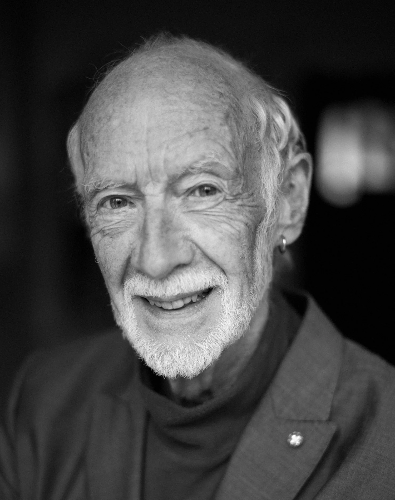 Elderly man with white beard smiling in black and white portrait.