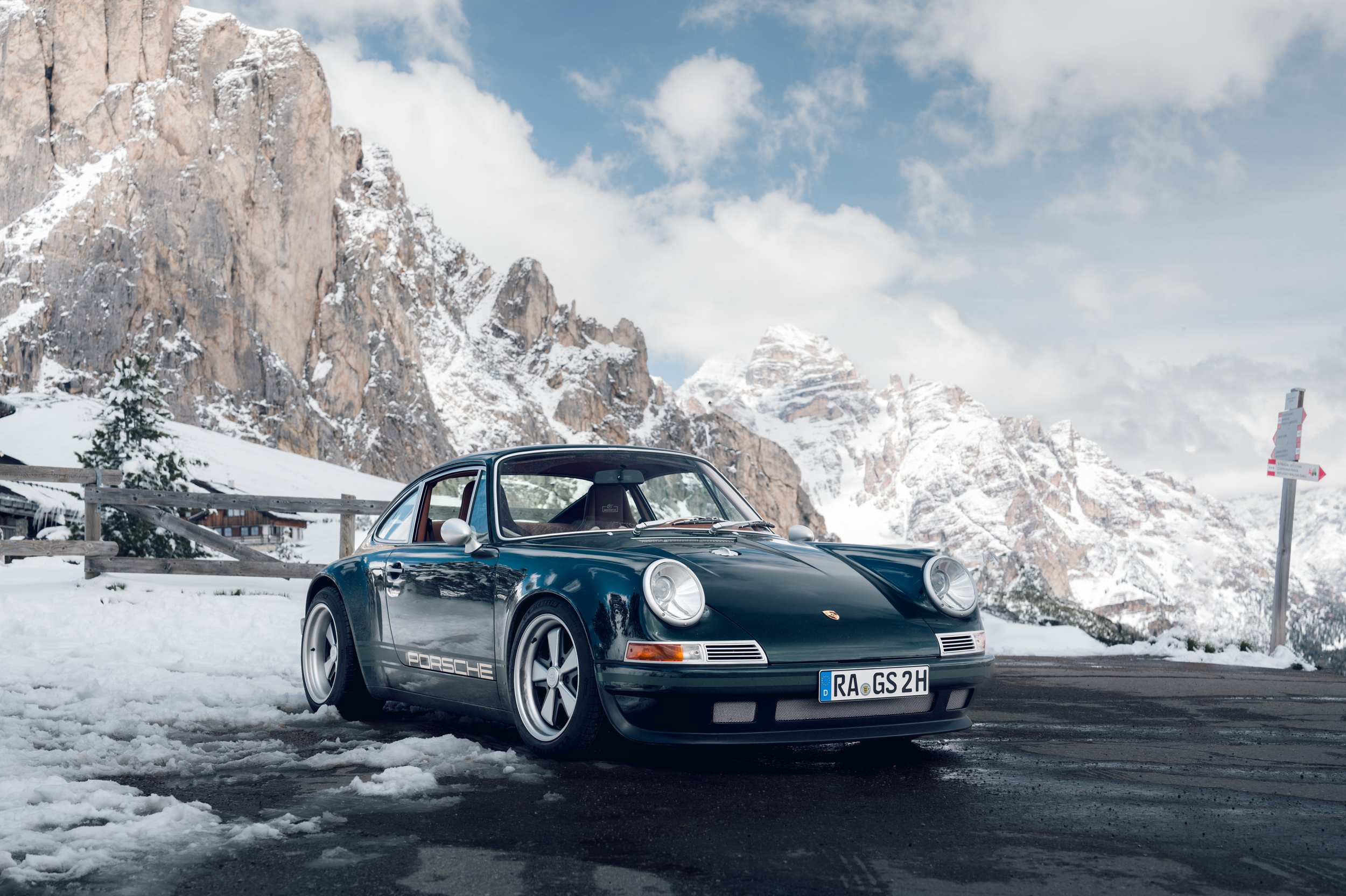 Ein schwarzer Porsche 911 vor schneebedeckten Bergen und einem bewölkten Himmel.