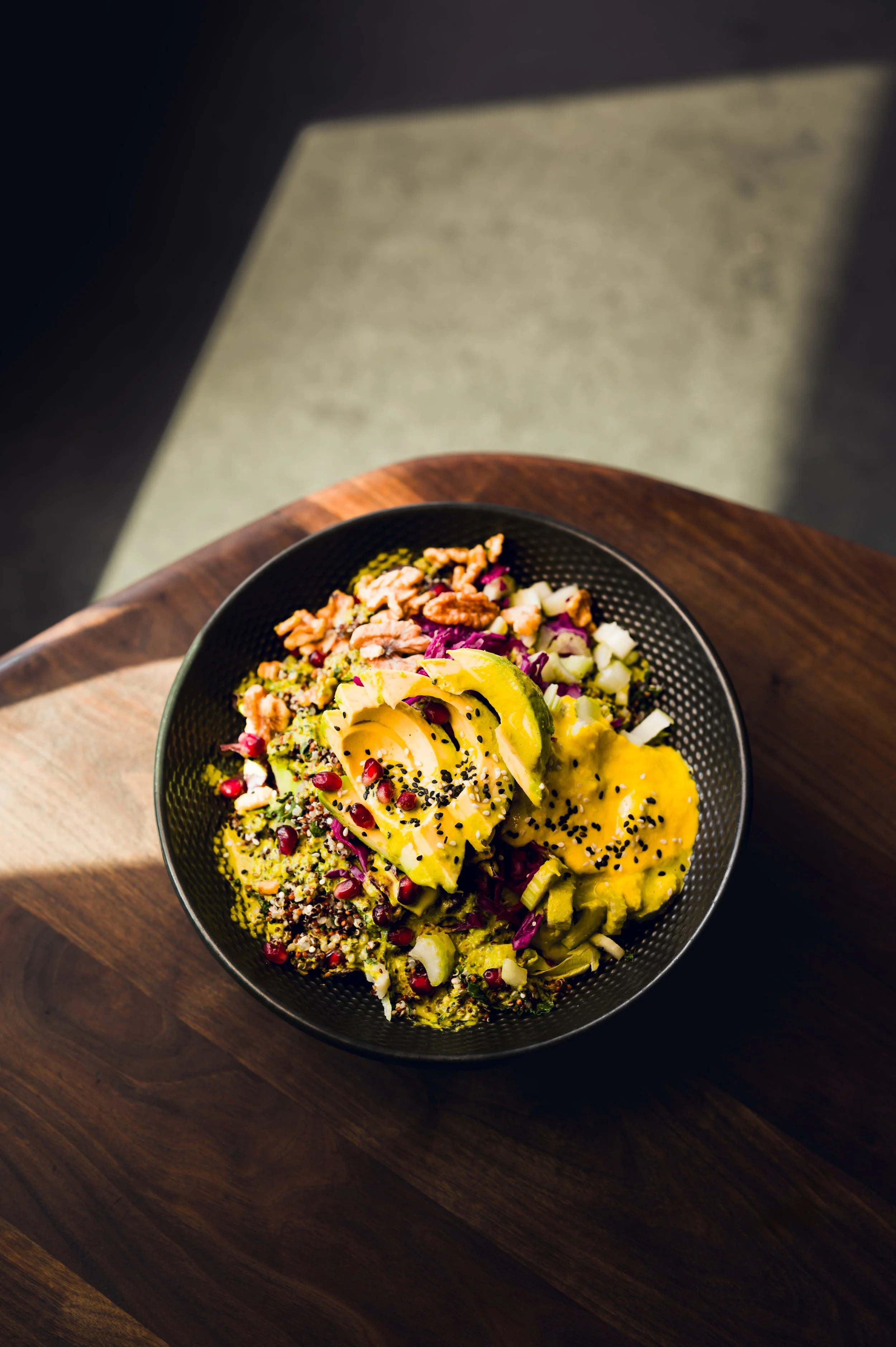 Schüssel mit gemischtem Salat, Avocado, Pomegranate, und Samen auf einem dunklen Holztablett im natürlichen Licht.