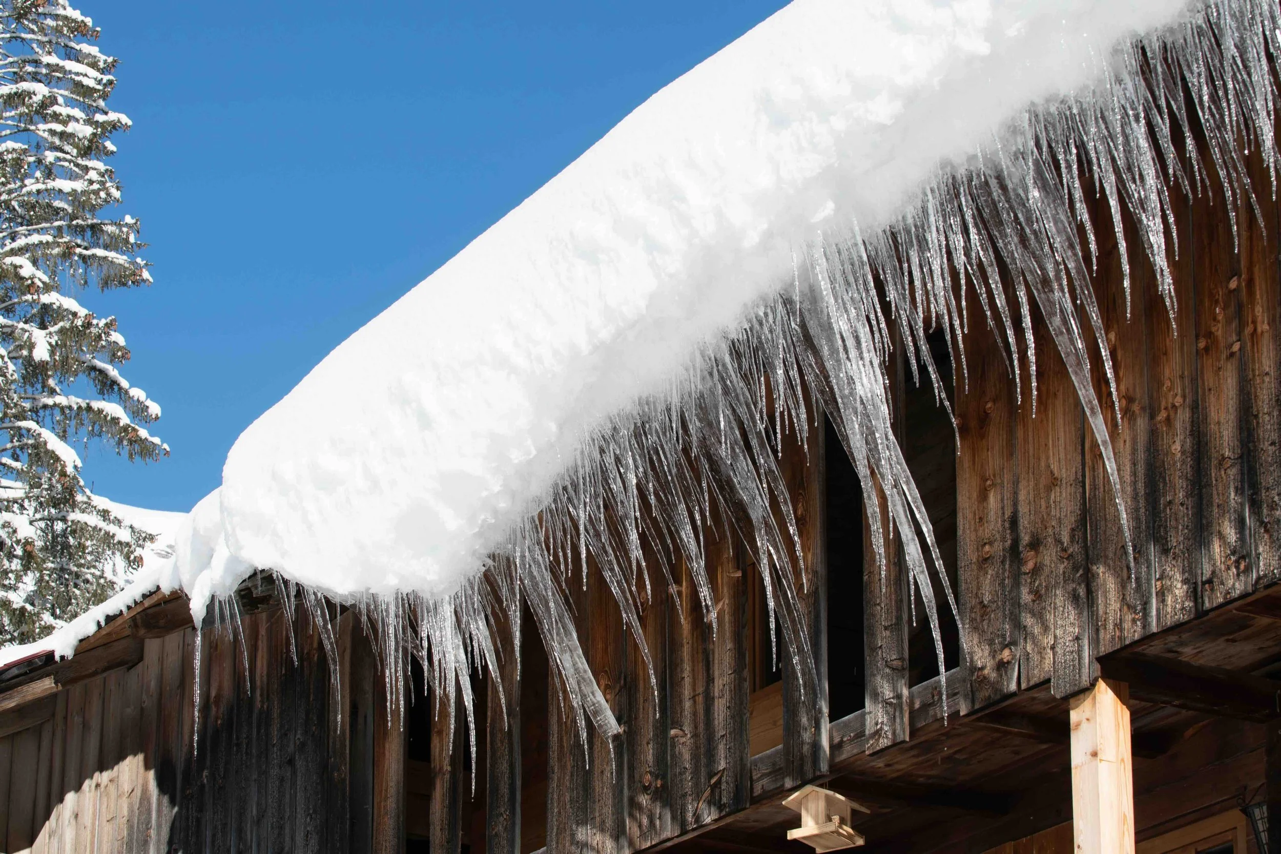 Gouttière d'un toit enneigé avec des stalactites de glace et un ciel bleu.