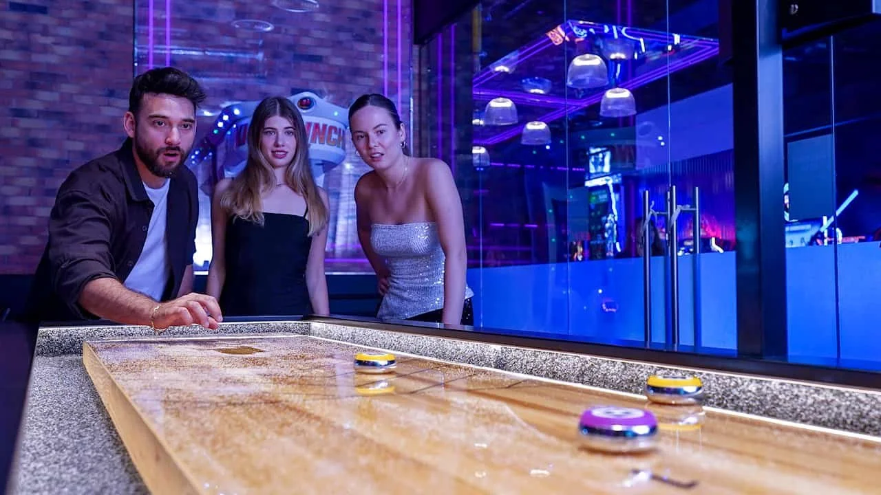 Three young adults gathered around a Supercharged Shuffleboard table in Hushh, Dubai