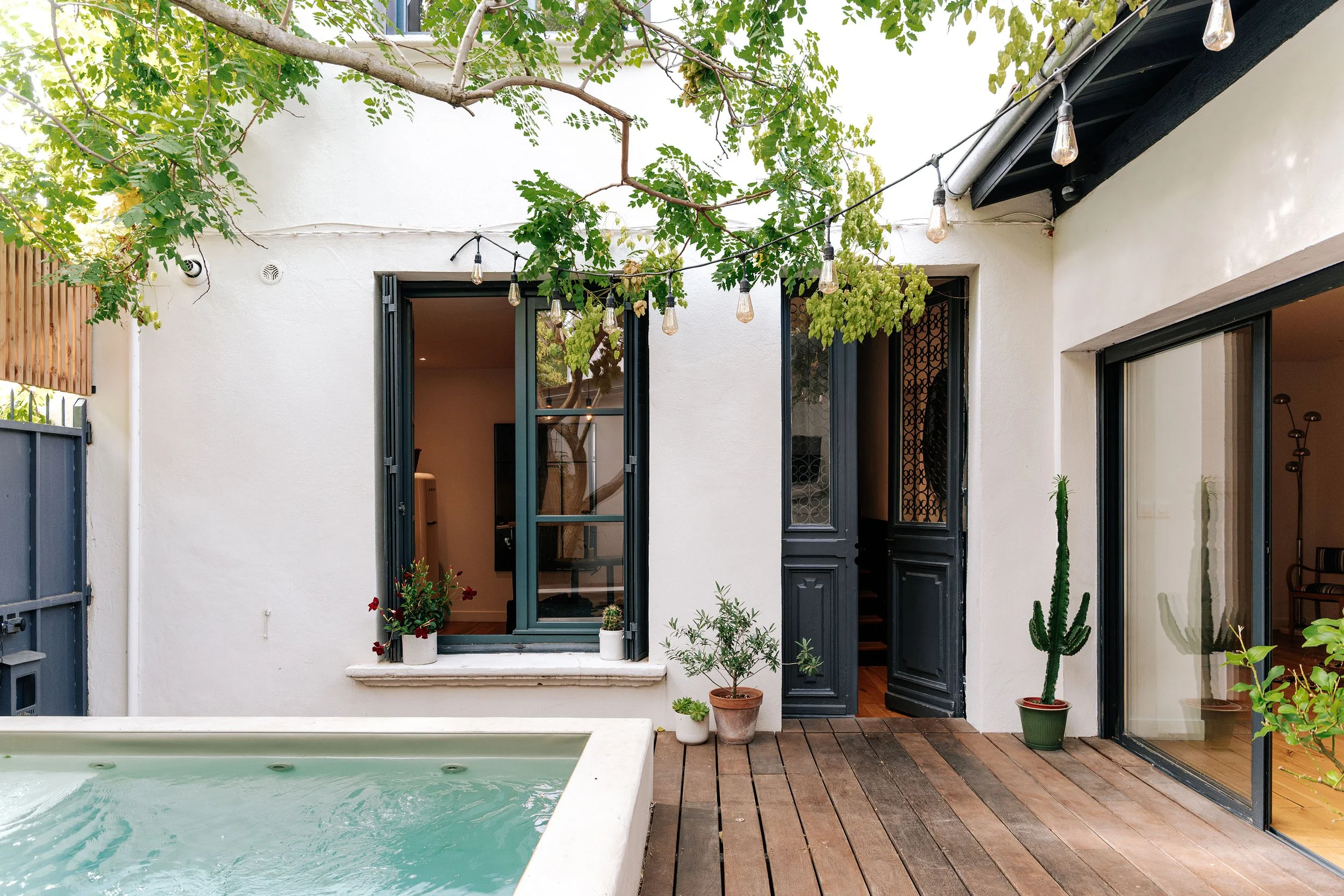 Façade rénovée ouverte sur un patio planté où cohabitent menuiseries contemporaines, bassin et terrasse en bois. Une cour intime qui devient la véritable pièce centrale de la maison.