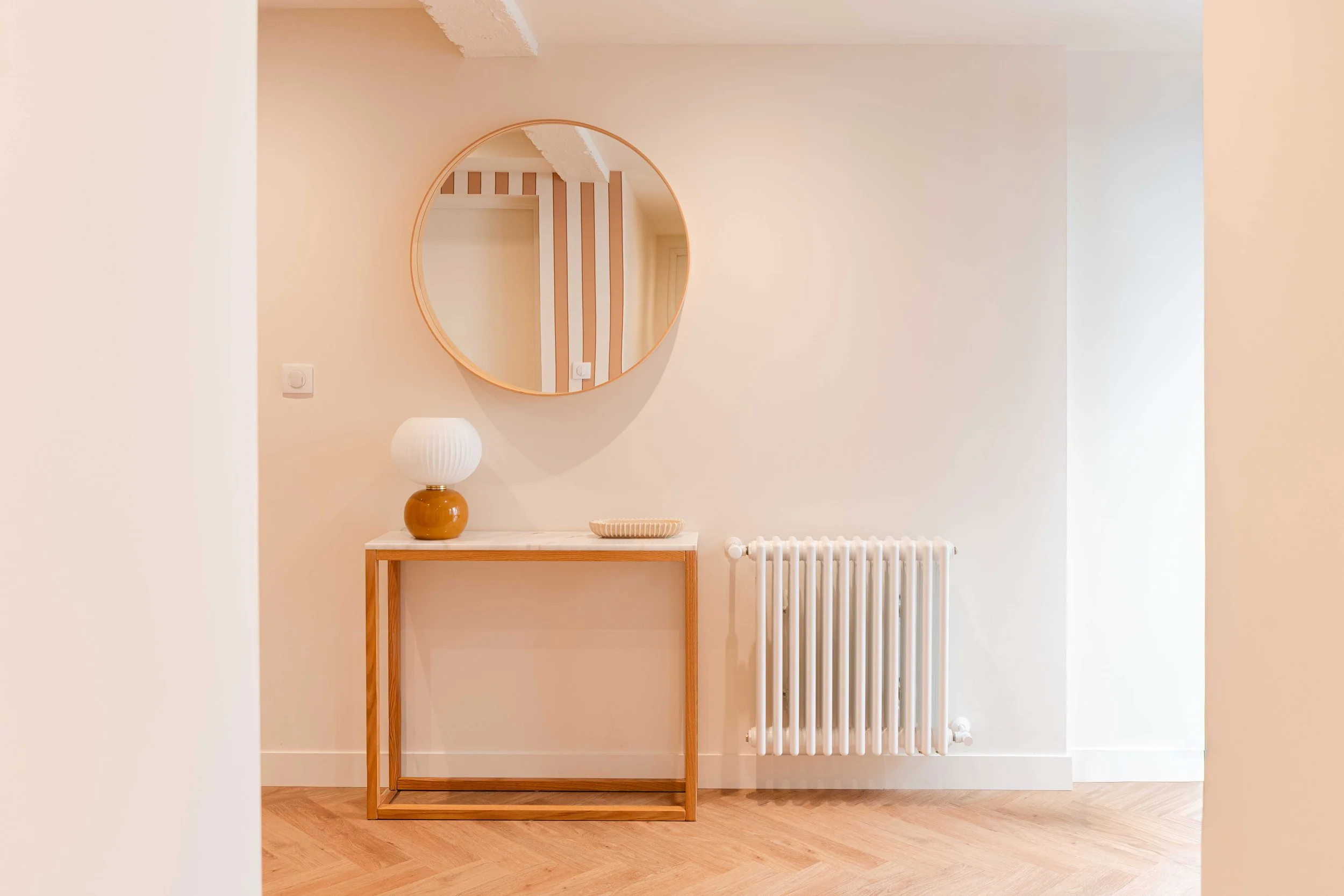 Vue frontale du meuble d’entrée de la maison l’Agly après rénovation. L’association entre bois naturel, miroir et radiateur en fonte souligne le dialogue entre contemporain et éléments d’origine. Atelier Kiso valorise la transformation de maisons an