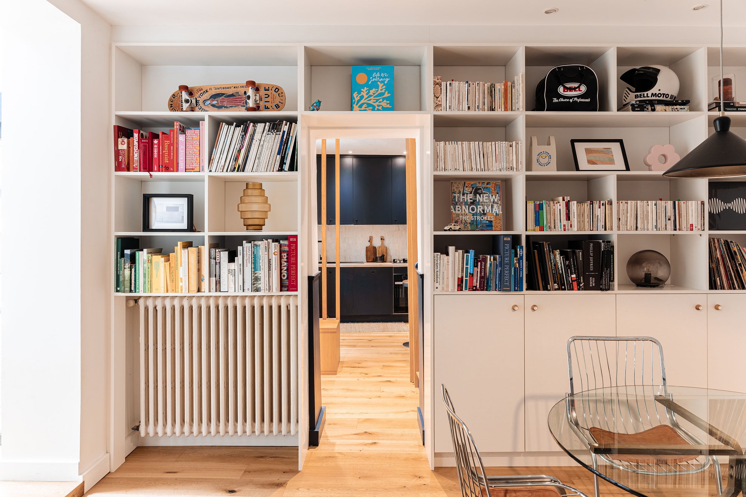 Bibliothèque en bois réalisée sur mesure et dessinée comme une cloison habitée. Elle structure les espaces, encadre les vues vers la cuisine et transforme le rangement en élément d'architecture.