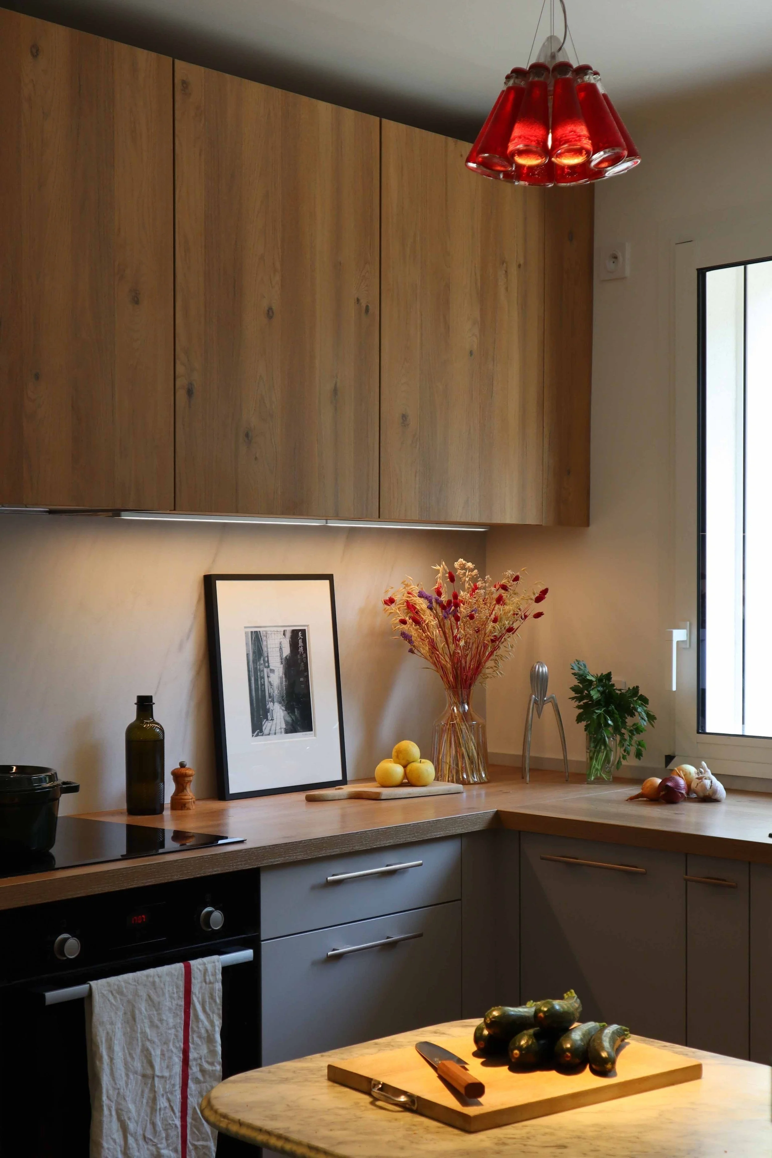 Réalisation d’une cuisine sur mesure avec façades et plan de travail en bois et suspension rouge dans la maison Uchi à Toulouse.