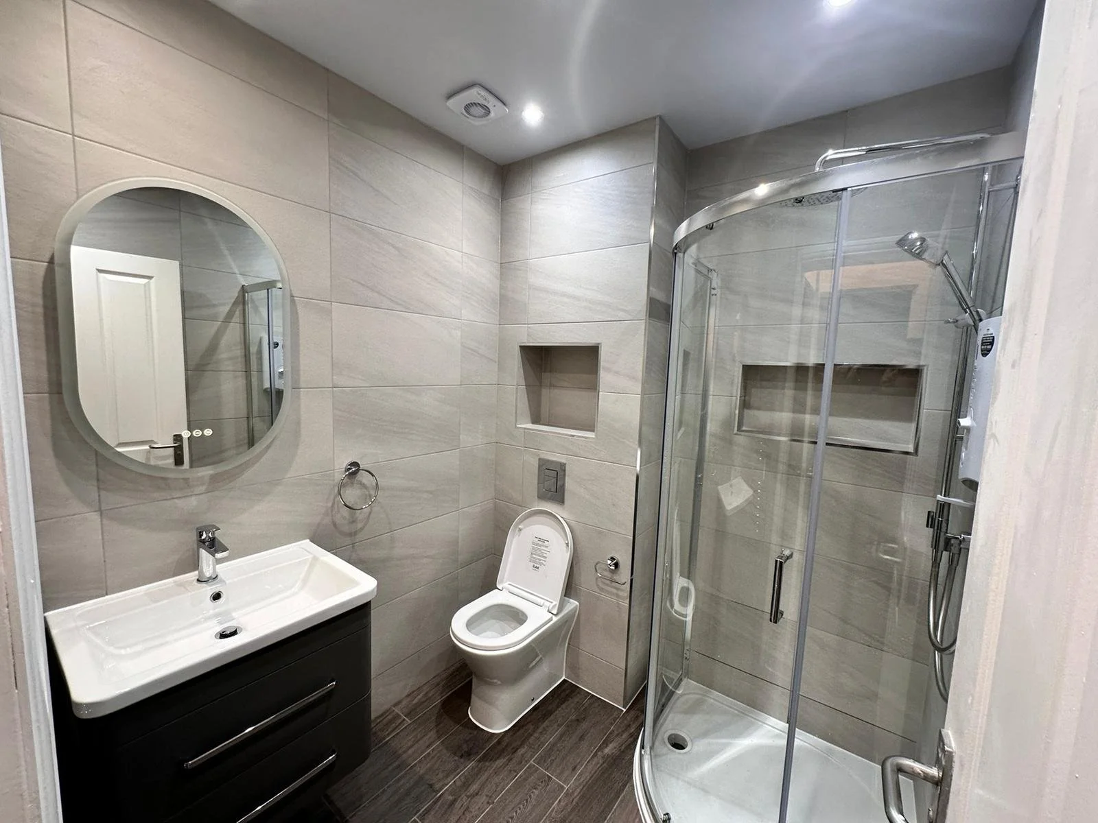 Modern bathroom with a white sink vanity, a toilet, a glass shower enclosure, and a wall mirror.