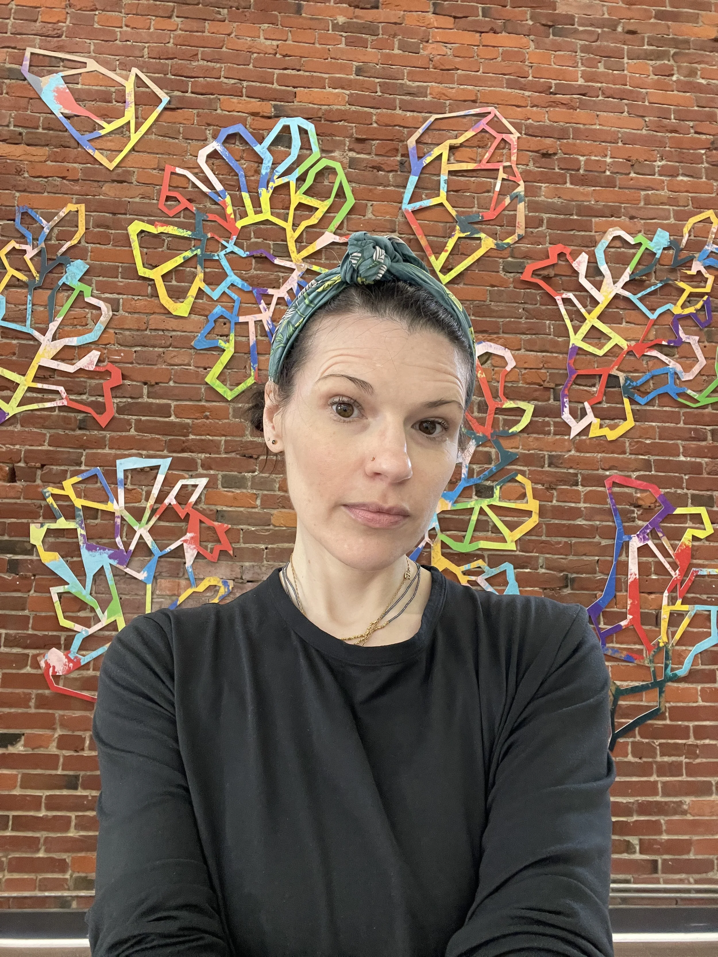 Artist Torea Frey standing in front of Wild Flowers installed on a brick wall at Slip Gallery in Seattle.