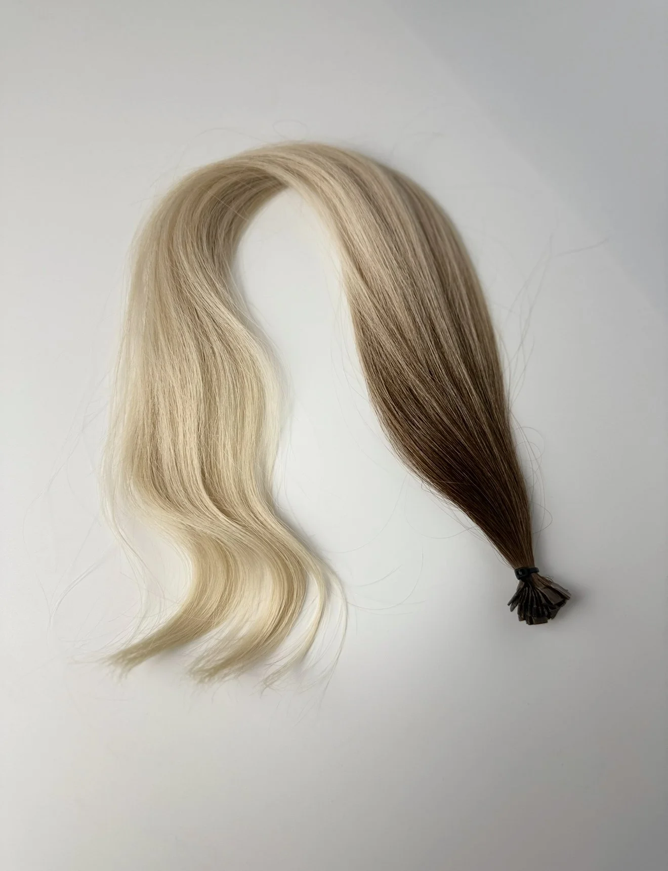 Stranded blonde hair extension with dark brown tips tied with a black rubber band