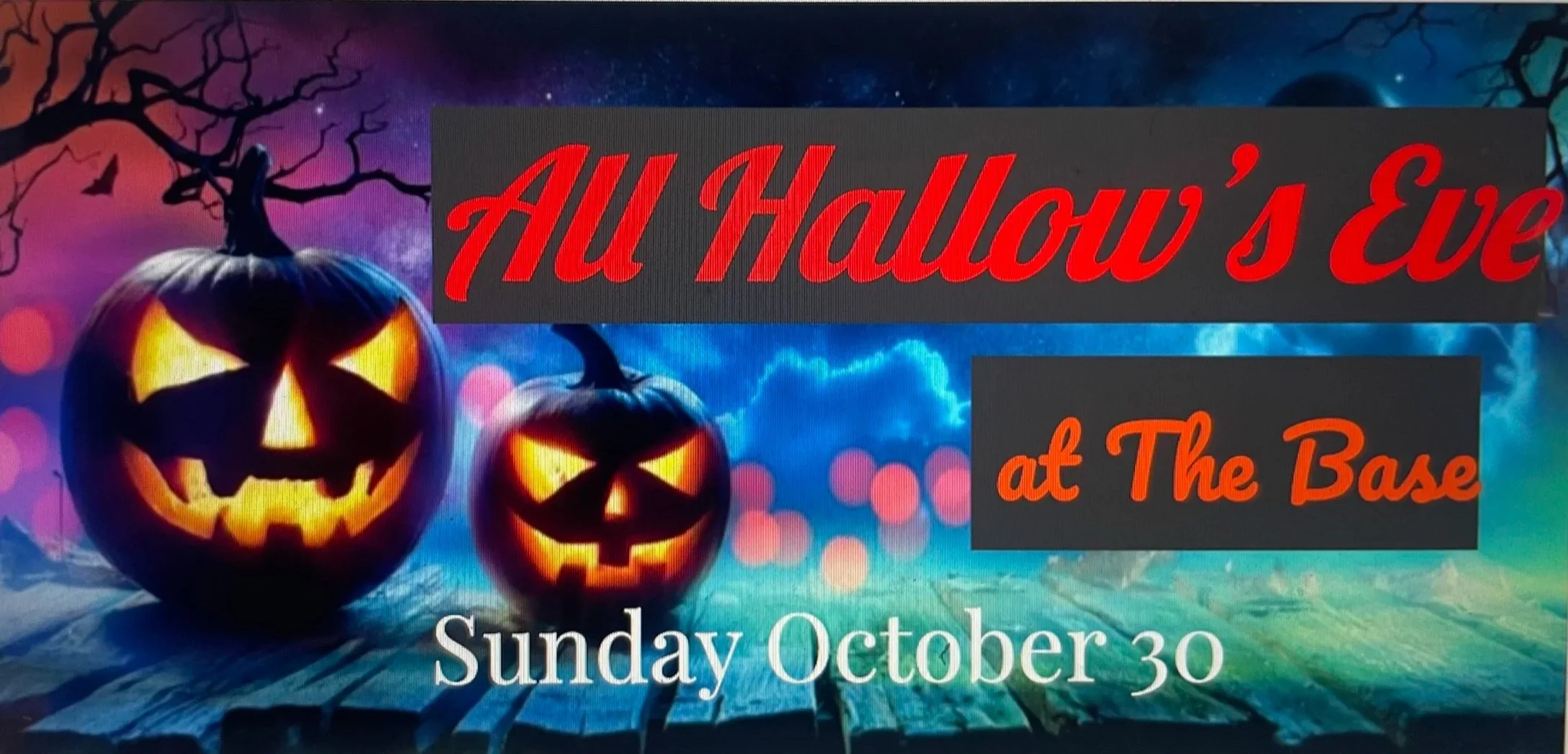 An advertisement for Halloween event featuring two carved pumpkins with glowing faces, a spooky background with ghostly clouds and a leafless tree, with text 'All Hollow's Eve at The Base' and 'Sunday October 30'.