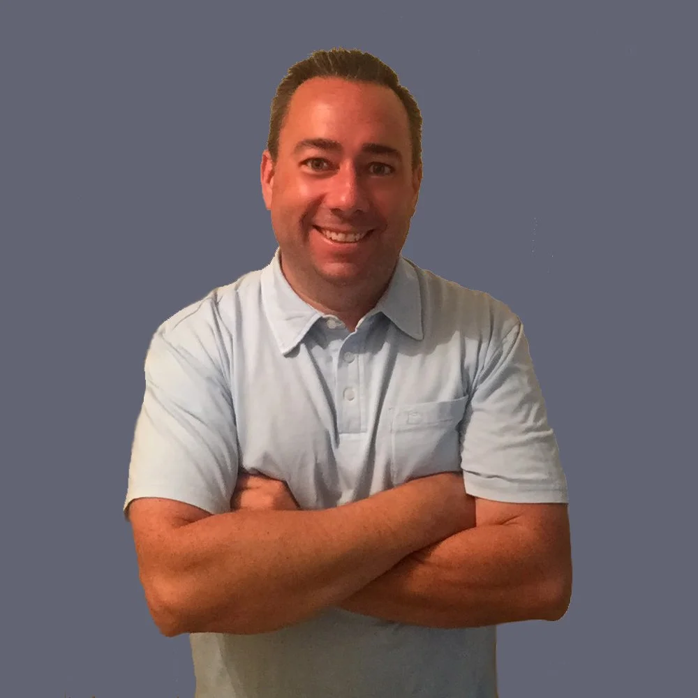 A smiling man with short brown hair, wearing a light gray polo shirt, standing with arms crossed against a plain gray background.