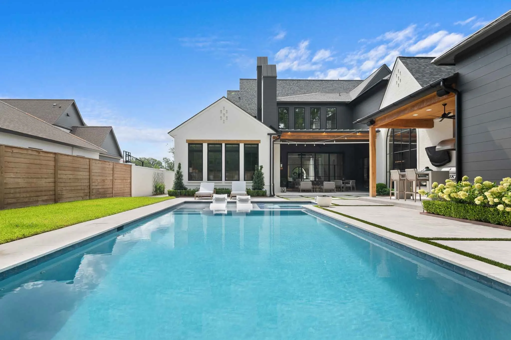 Modern backyard with a swimming pool, lounge chairs, a grill area, and a spacious patio.