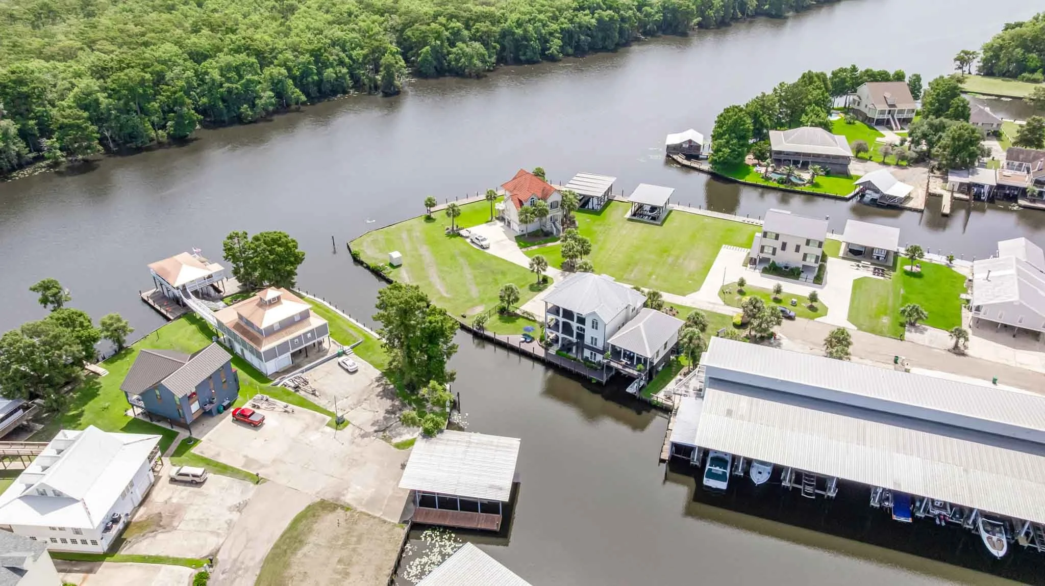 Aerial view of a residential waterfront neighborhood with houses, docks, boats, and lush green trees along a river.