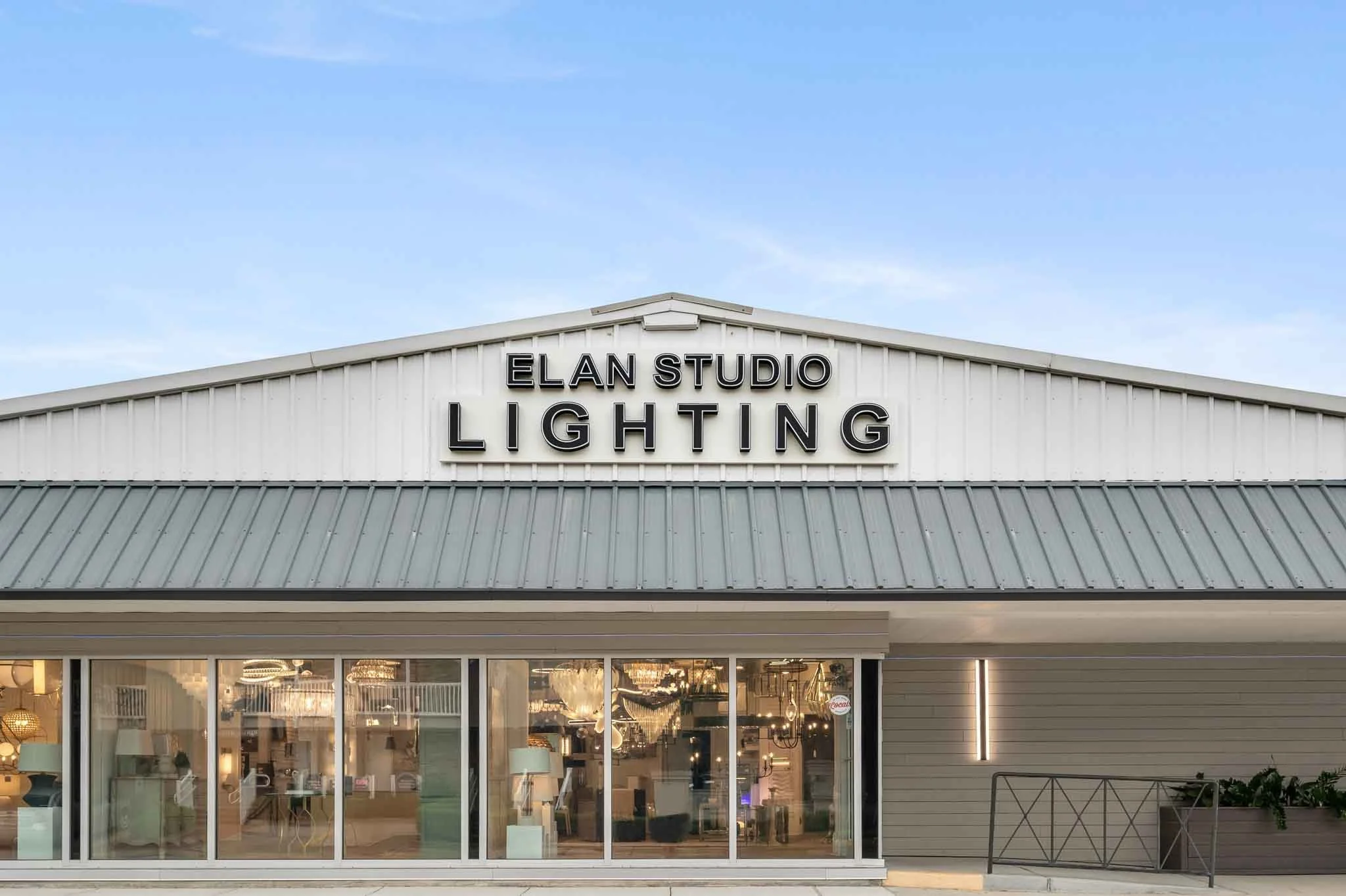 The front of a lighting store named ELAN STUDIO LIGHTING with large glass windows displaying chandeliers inside and a clear sky above.