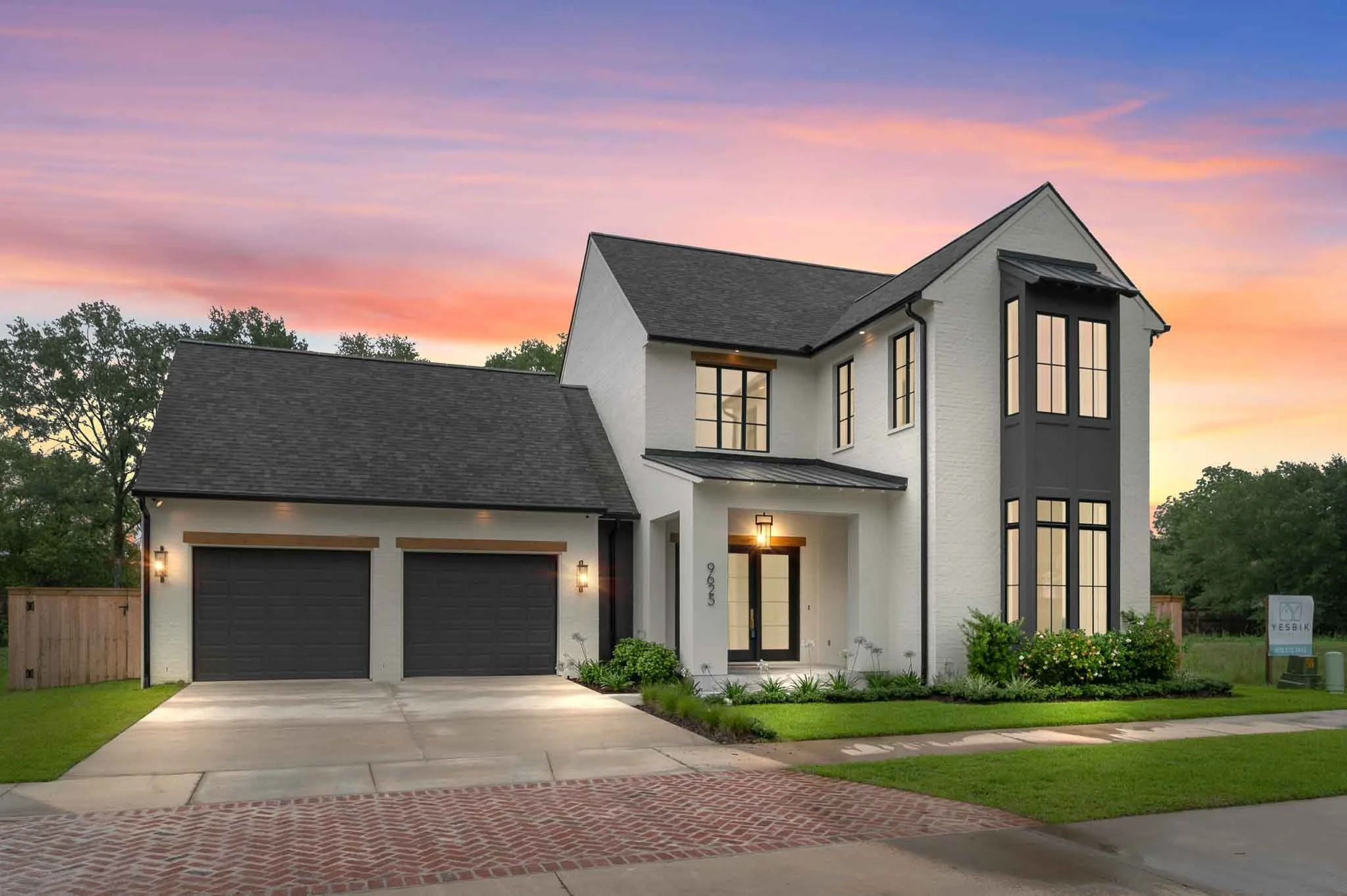 Modern two-story house with white exterior, black window frames, two-car garage, and a manicured lawn at sunset.