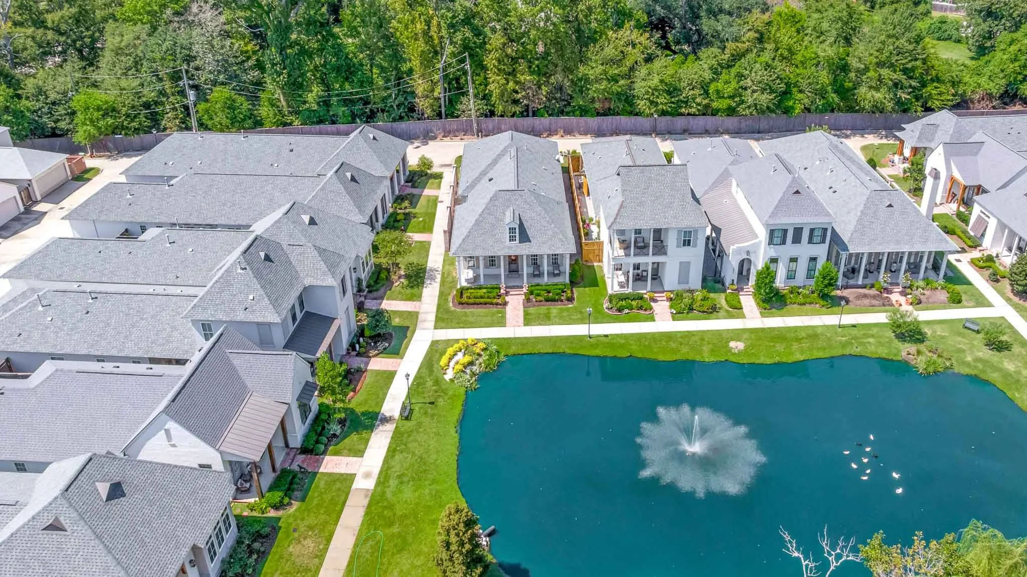 Aerial view of a residential neighborhood with houses, a pond with a fountain, and green lawns.