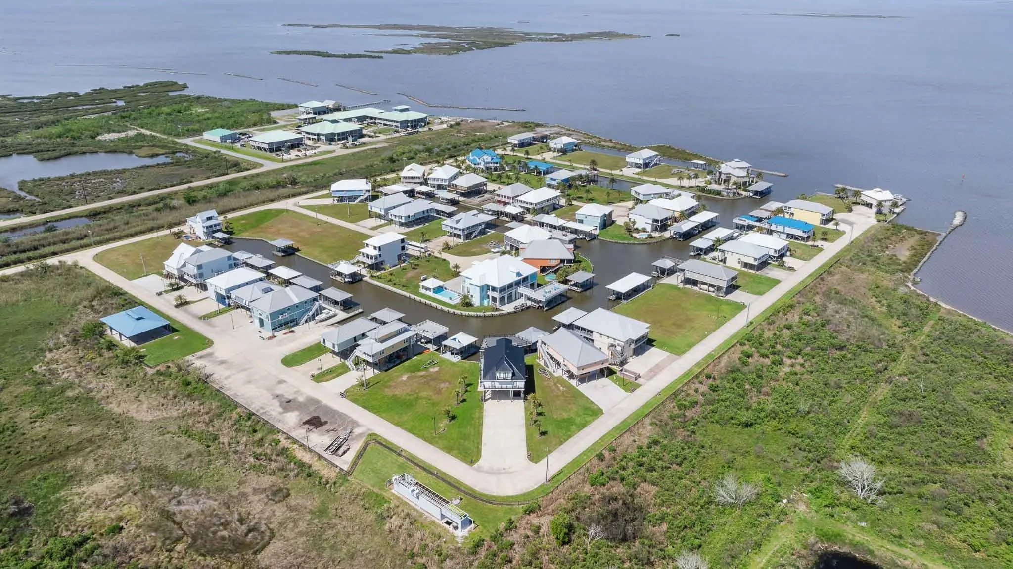 Aerial view of a waterfront residential community with multiple houses and canals on a peninsula surrounded by water and greenery.