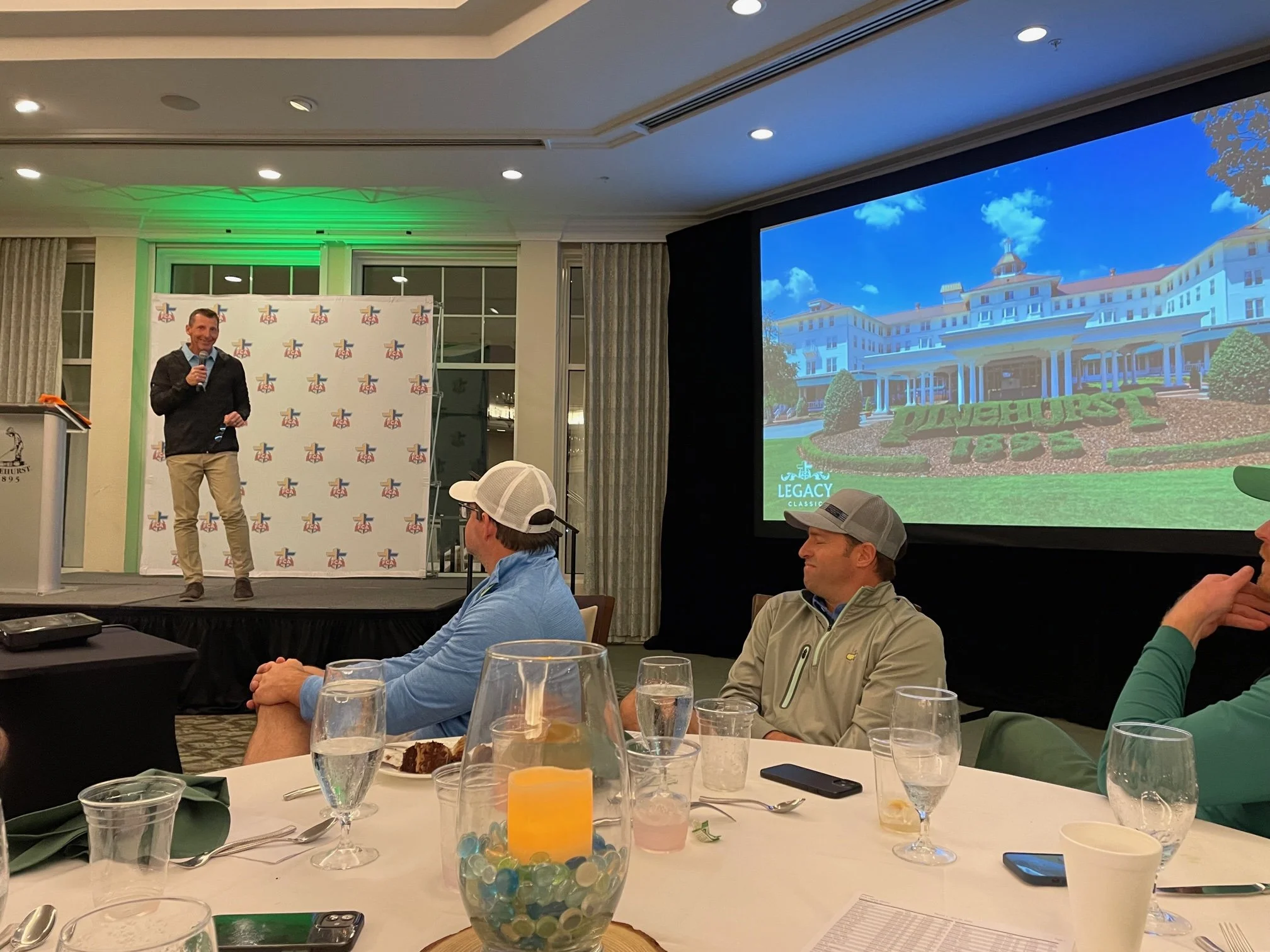 Speaker presenting at Legacy Golf donor banquet – guests seated for dinner during an evening of impact, celebration, and giving.