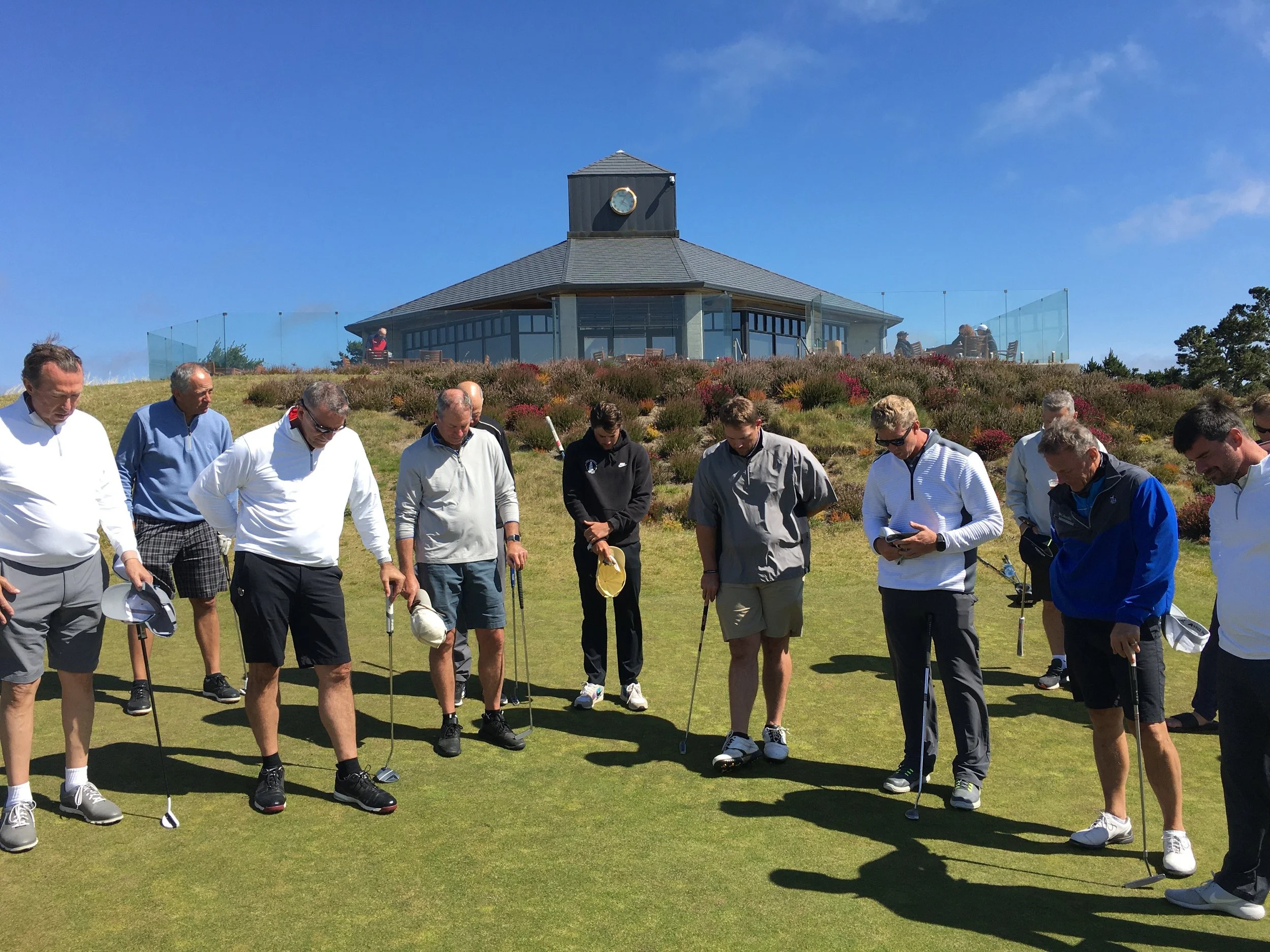 Group of men gathered on the green during a donor golf event, with a clubhouse in the background – reflecting, connecting, and enjoying a meaningful day on the course.