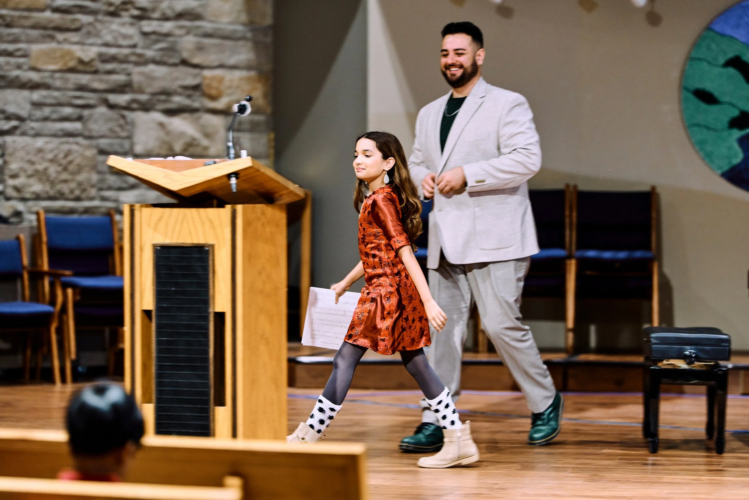 Sophiya confidently walking off stage after her piano recital performance as her teacher, Soroush, smiles at her.