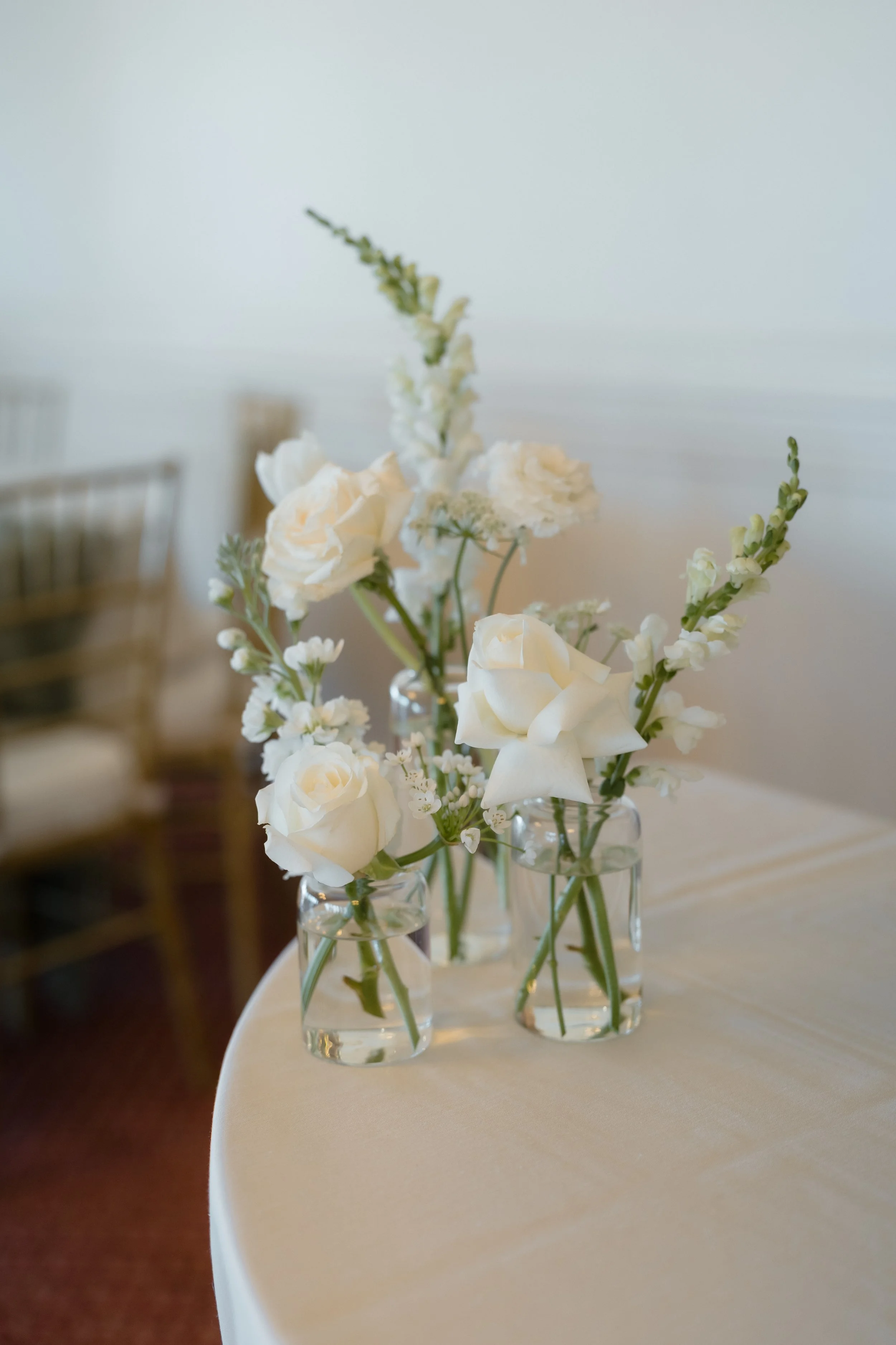 A close-up of several small glass vases with white flowers on a white tablecloth.
