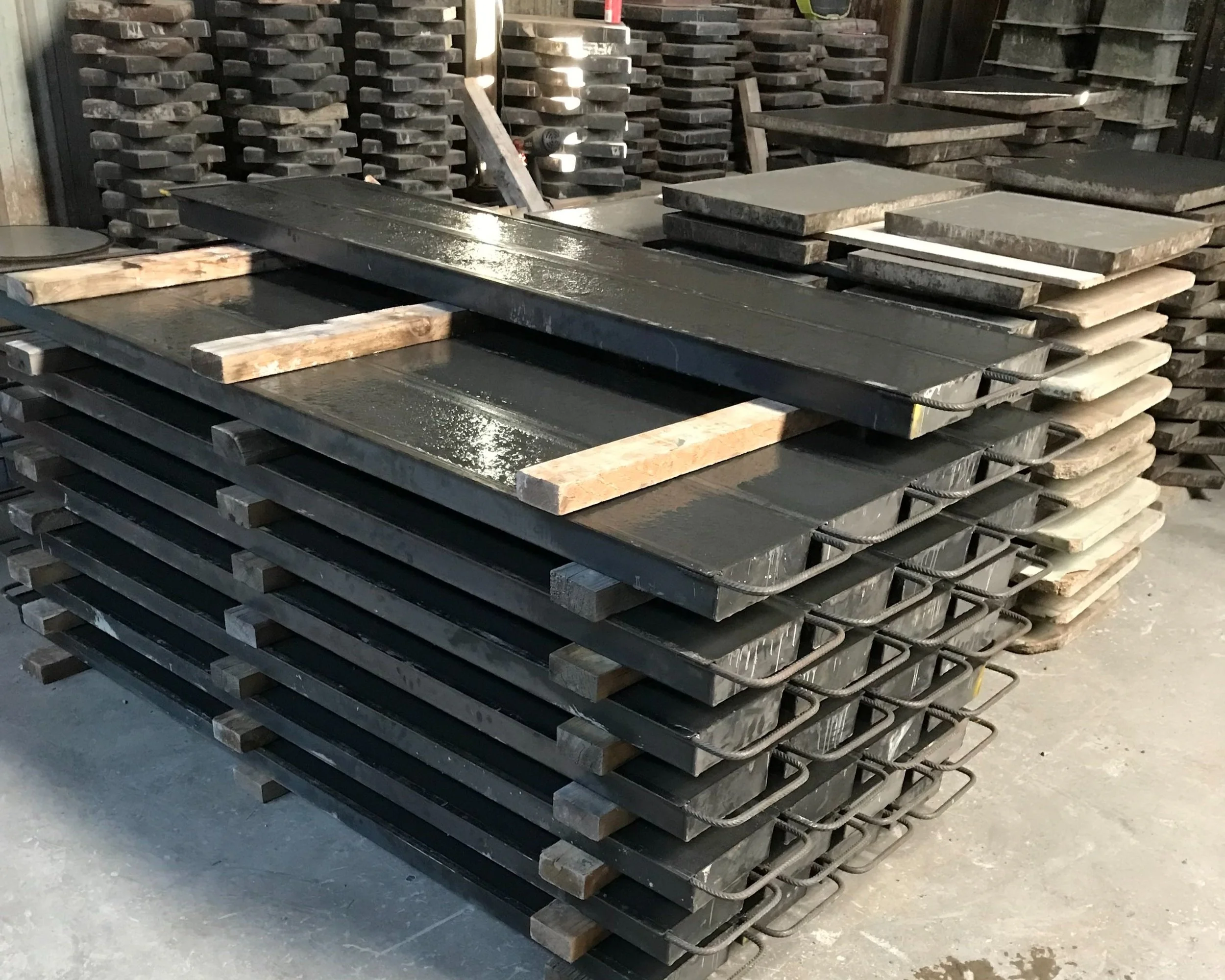 Stacks of black and grey metal moulds for pre-cast concrete production in factory setting.