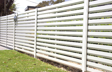 White horizontal slat fence with green grass in front and trees in the background.