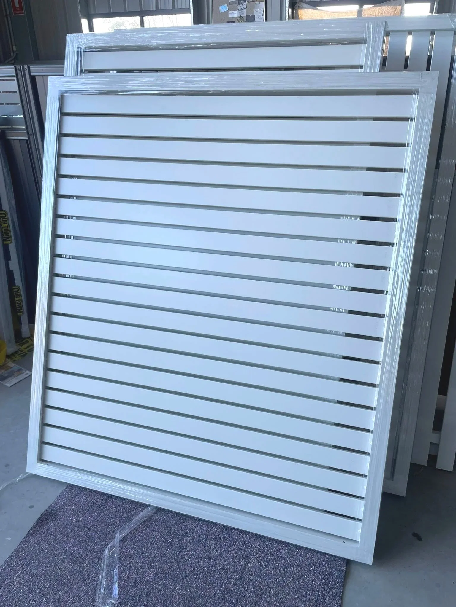 White slatwall display panels stacked upright in a store or warehouse, with a textured carpet in front.