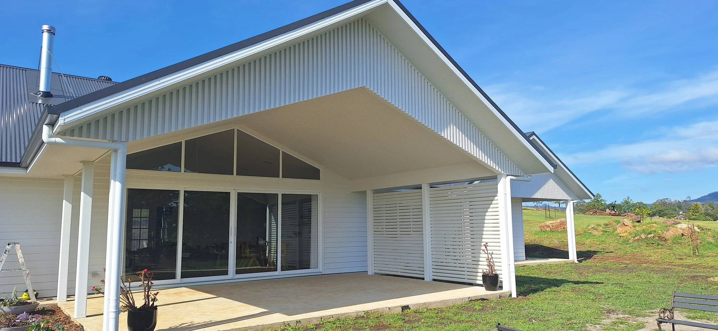 Modern house with white exterior, large glass sliding doors, and a covered patio area, situated in a grassy landscape with blue sky.