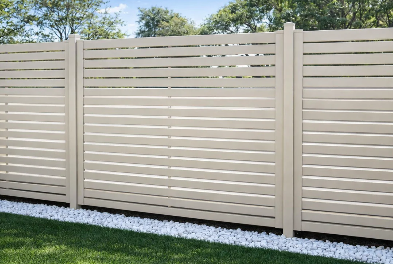 A white horizontal slat fence with white gravel underneath and green grass in the foreground, with trees and blue sky in the background.