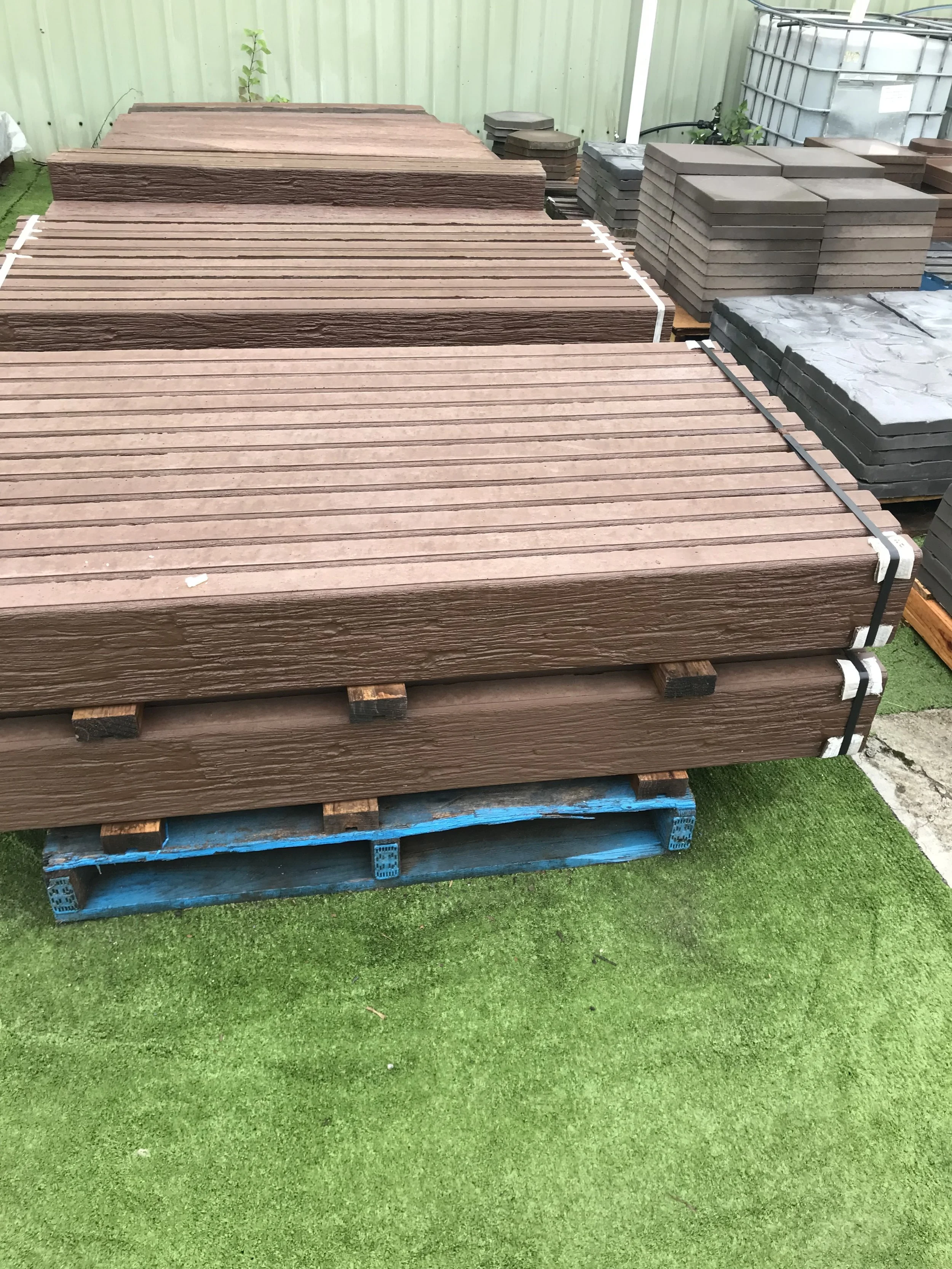 Stacks of brown timber grain concrete sleepers on wooden pallets outside on artificial grass.