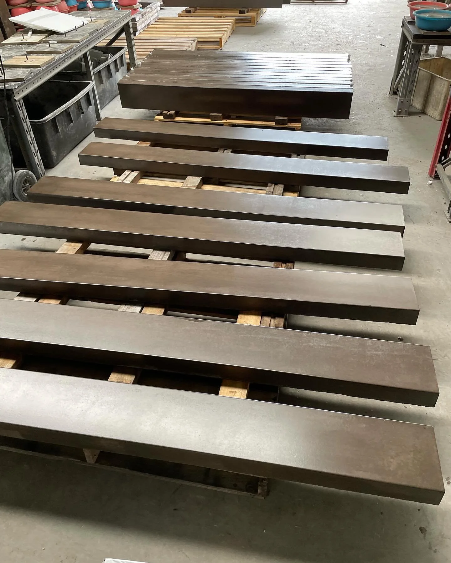 Several concrete sleepers of various shades of brown laid out on pallets in a workshop or warehouse.
