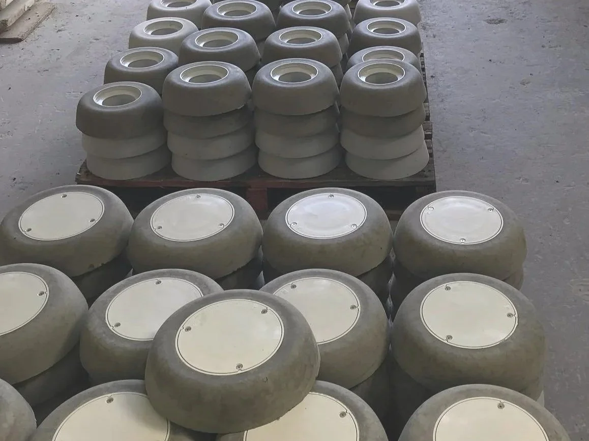 Multiple plumbing fittings with concrete surrounds. They are arranged in stacks on pallets in an outdoor area.