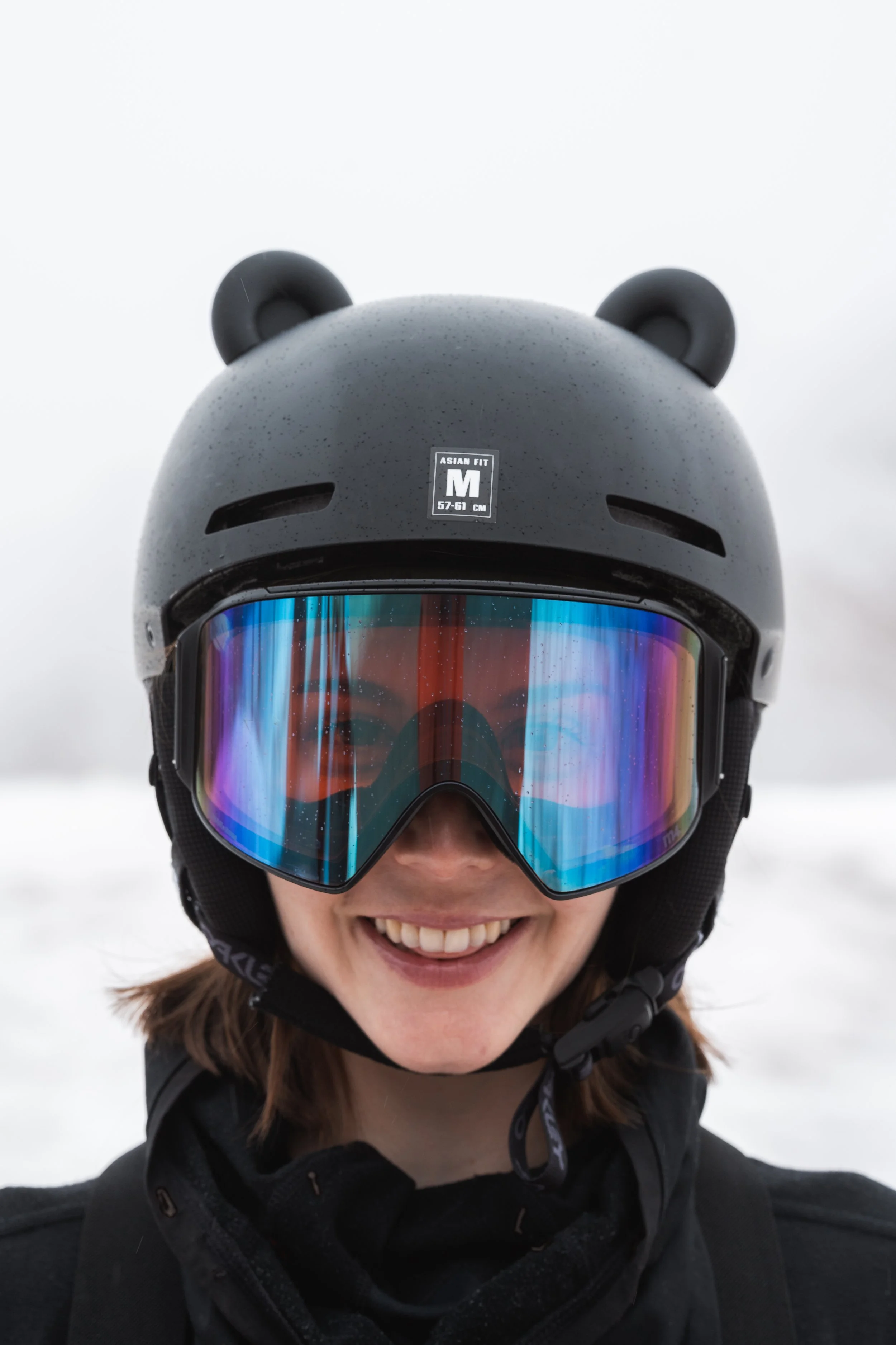 Black snowboard helmet with 3D printed bear ears on a snowy mountain