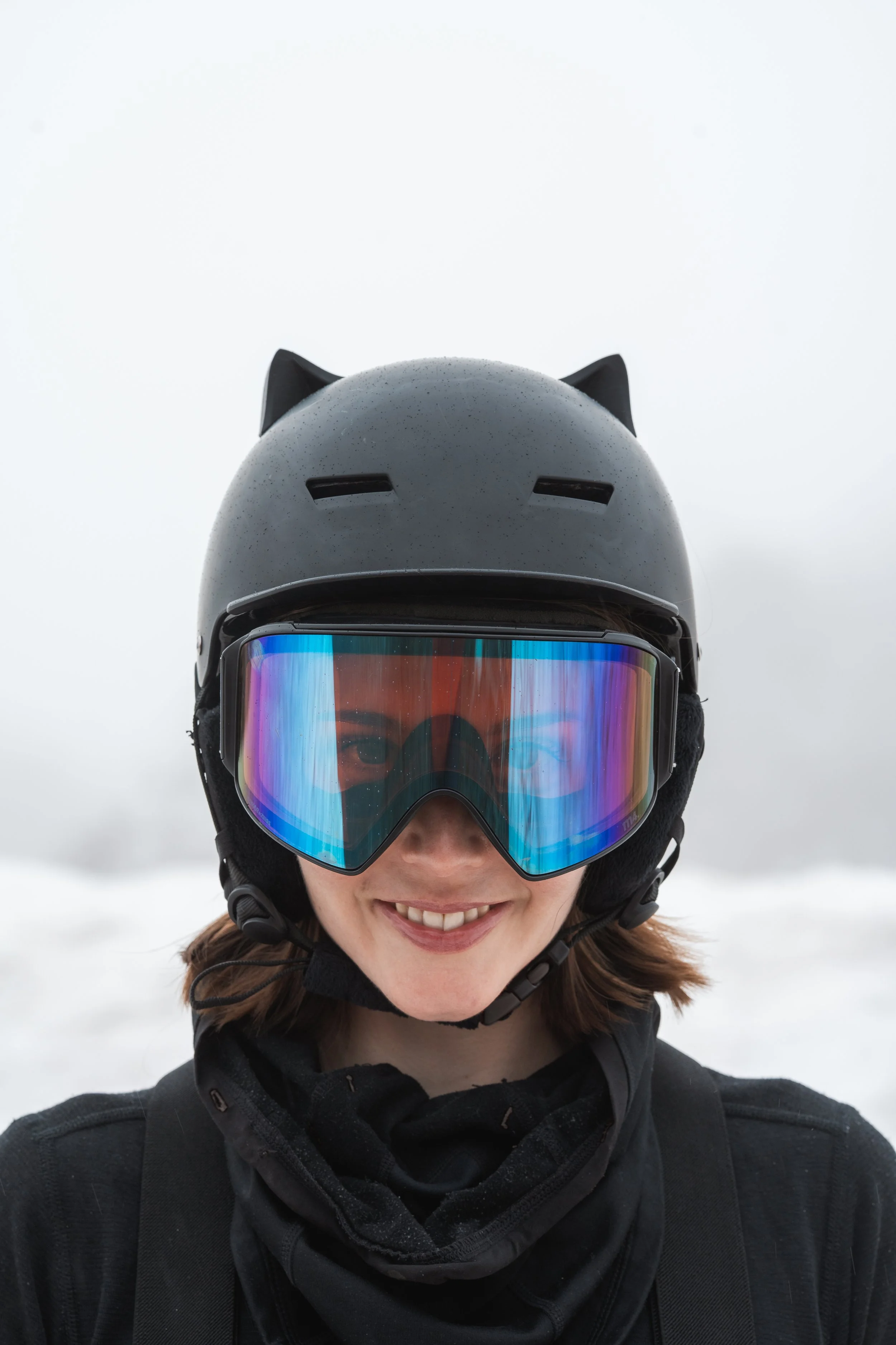 Black snowboard helmet with 3D printed cat ears on a snowy mountain