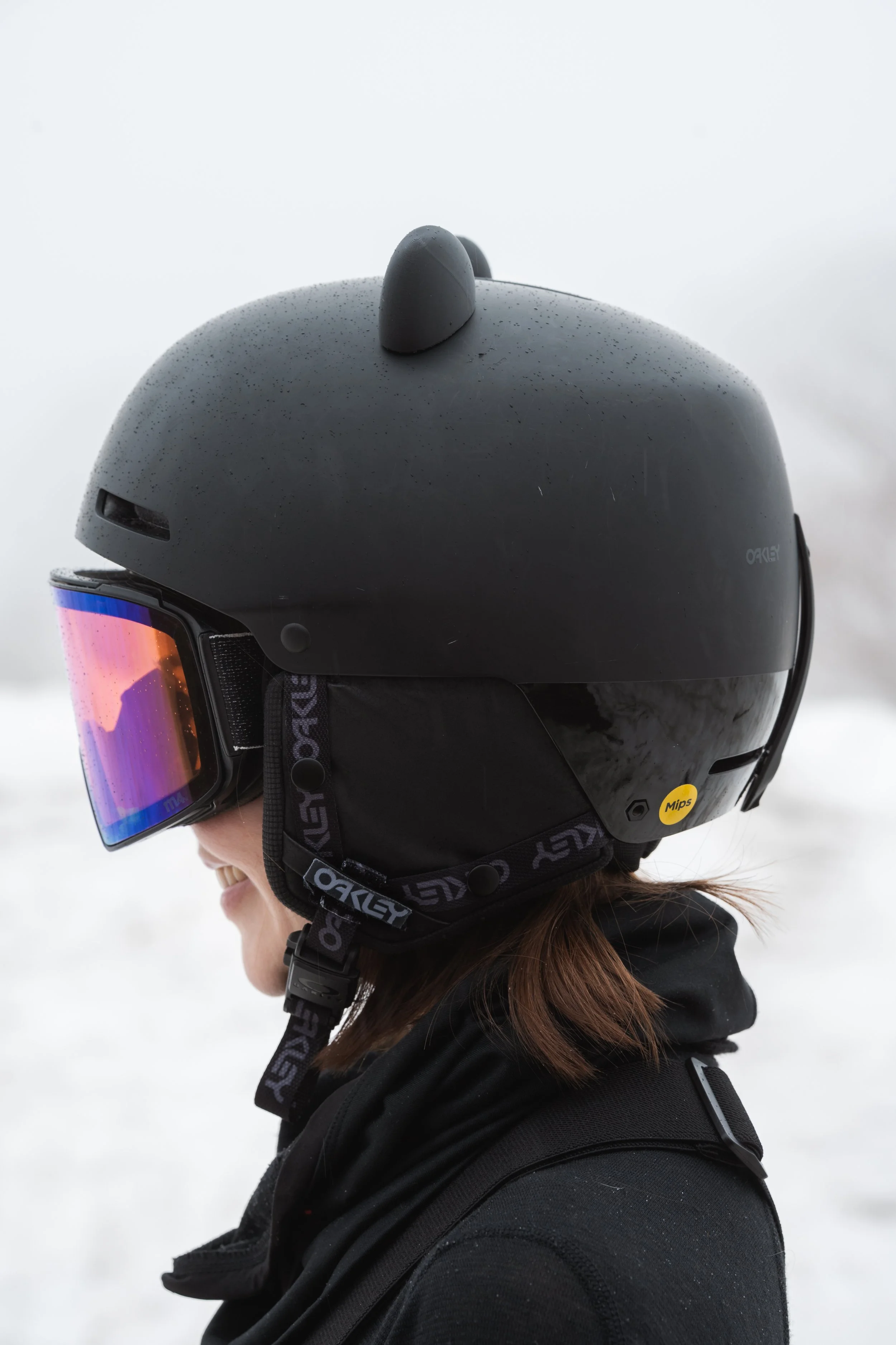 Black snowboard helmet with 3D printed bear ears on a snowy mountain