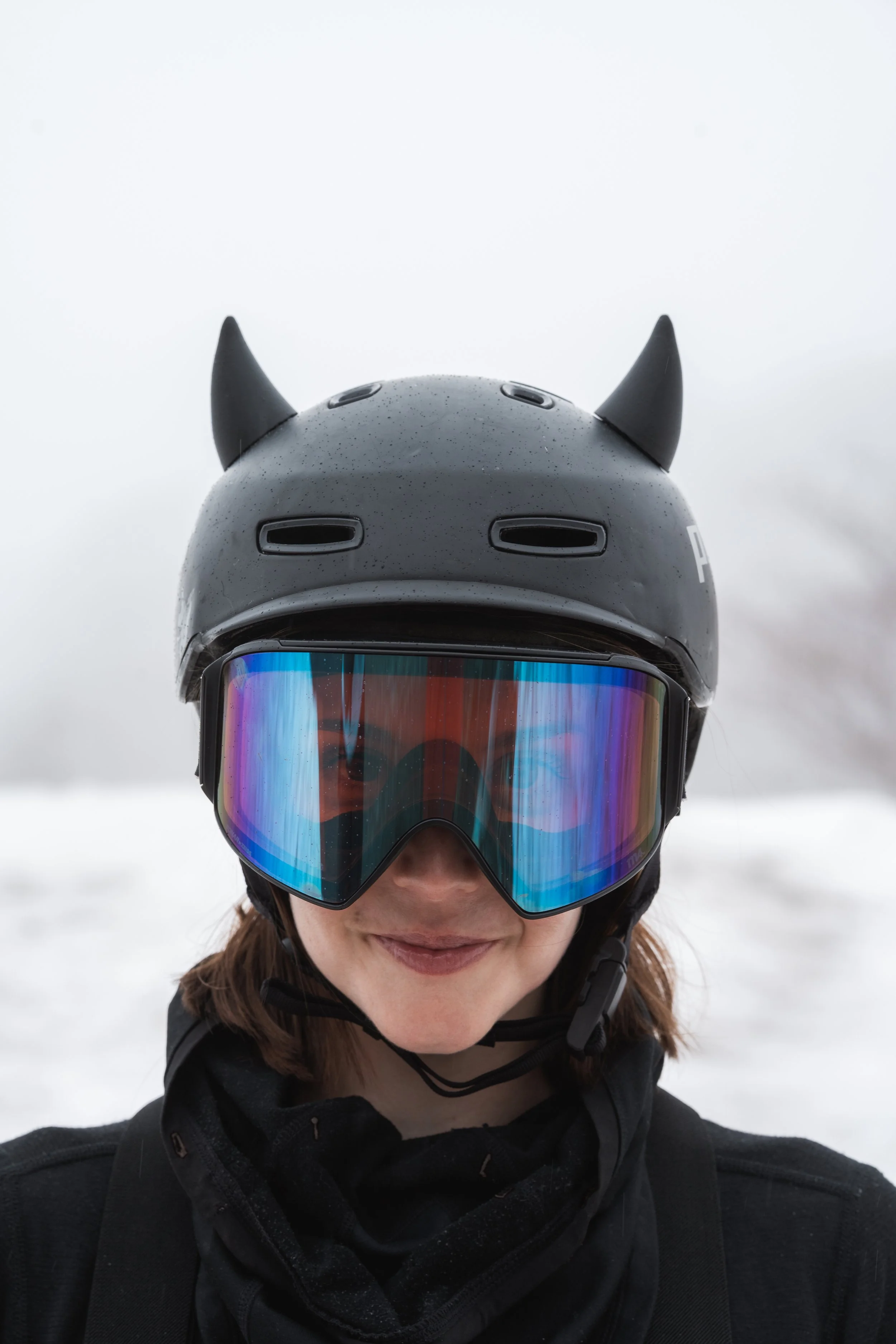 Black snowboard helmet with 3D printed horn ears on a snowy mountain