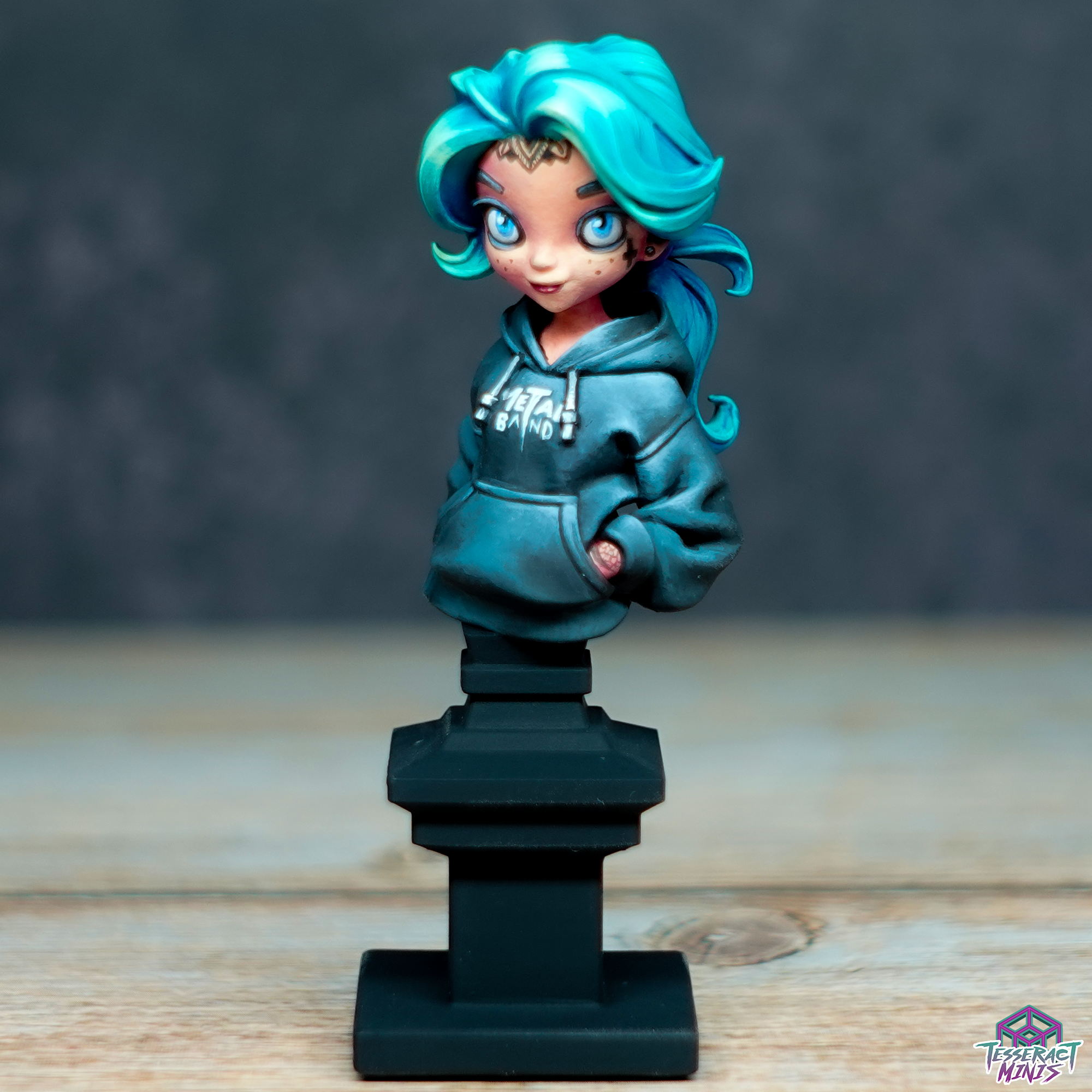 A stylized collectible figurine of a girl with turquoise hair and blue eyes, wearing a dark gray hoodie with 'Metal Band' written on it, standing on a black pedestal against a neutral background.