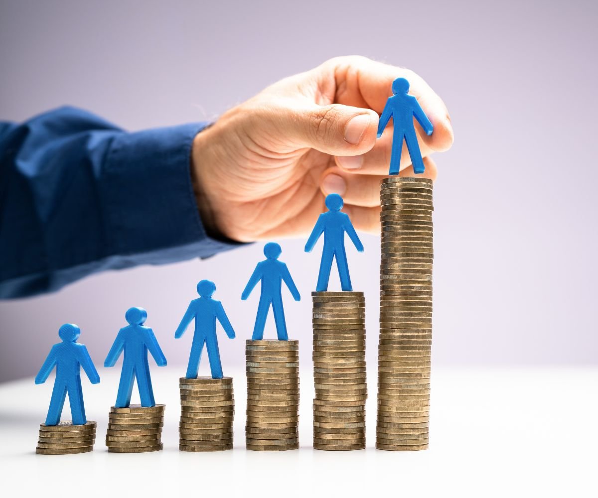 The new government budget - close up of a man's hand placing blue figures onto 6 piles of coins increasing in height