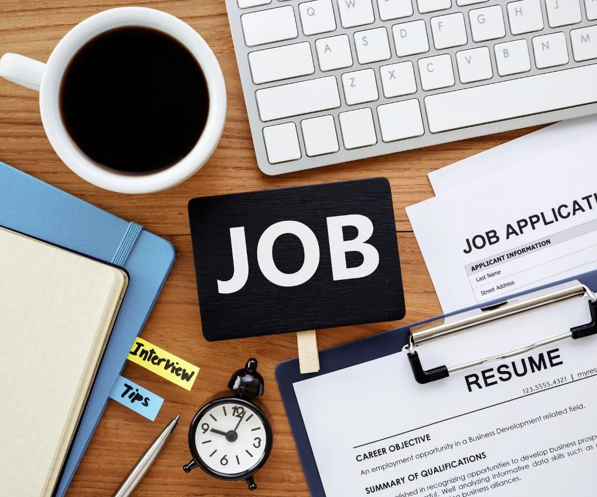 Stay resilient - a cluttered desk with coffee, files, CV, job applications, alarm clock and laptop on it