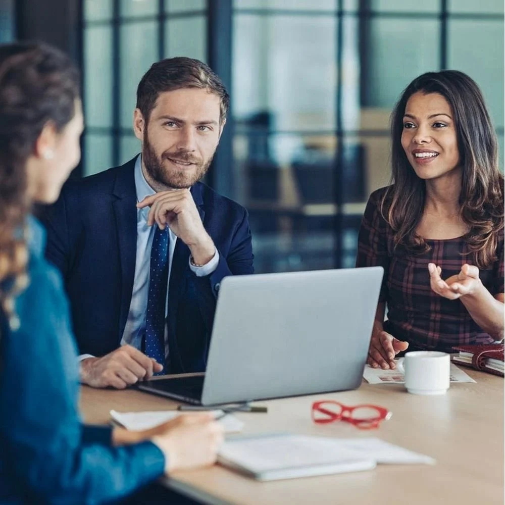 3 business people sat around a desk with an open laptop in discussion on how to navigate staffing