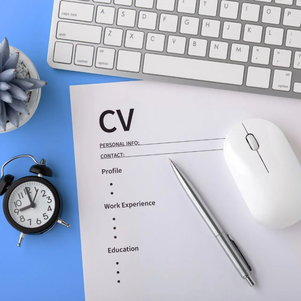 Energise your job searching with a great CV like this one on a blue desk with a computer keyboard, mouse, pen and clock