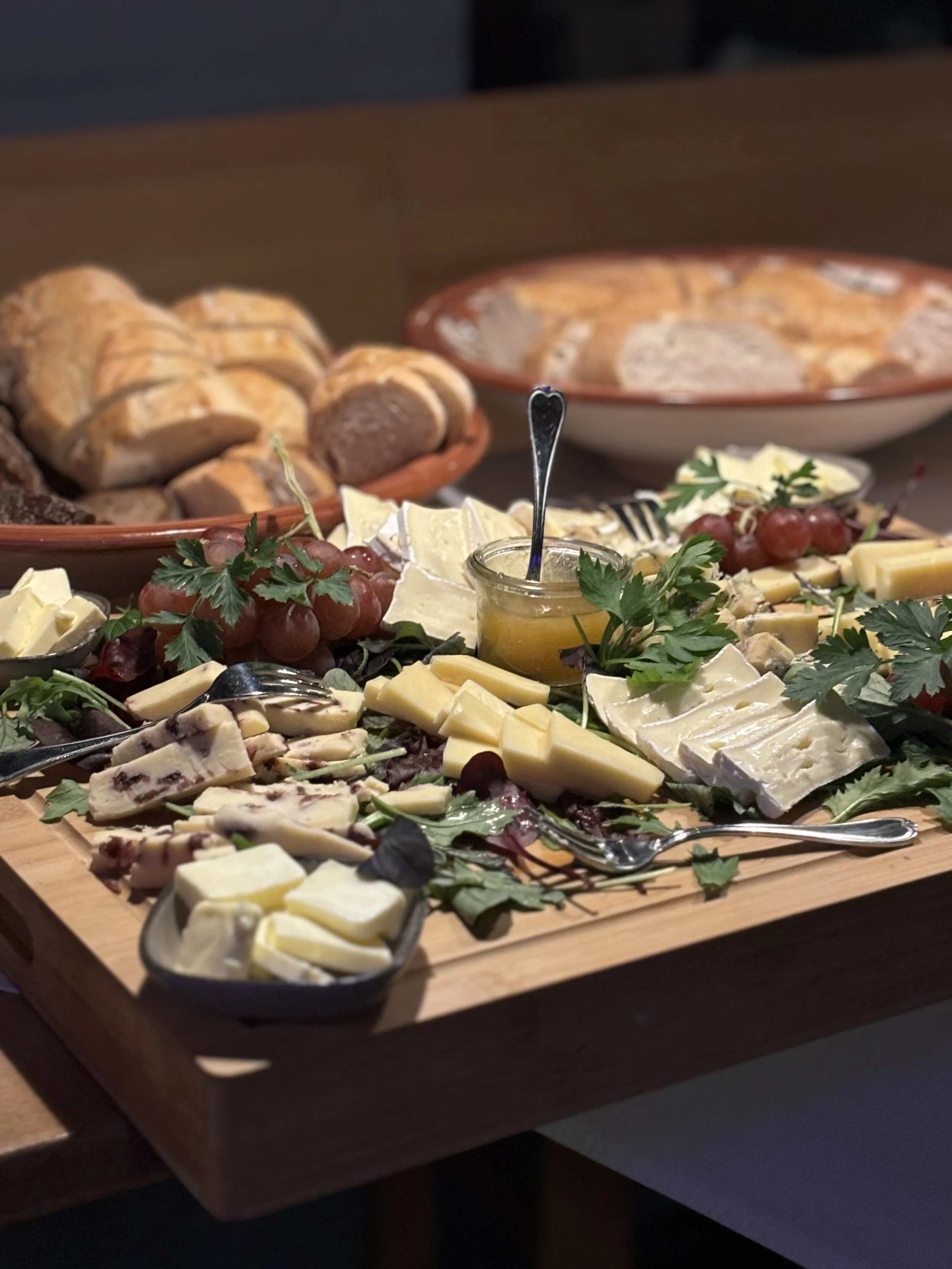 Brett mit einer Käsevariation, Trauben und Frischbrot, im Hintergrund eine Schüssel mit Suppe.