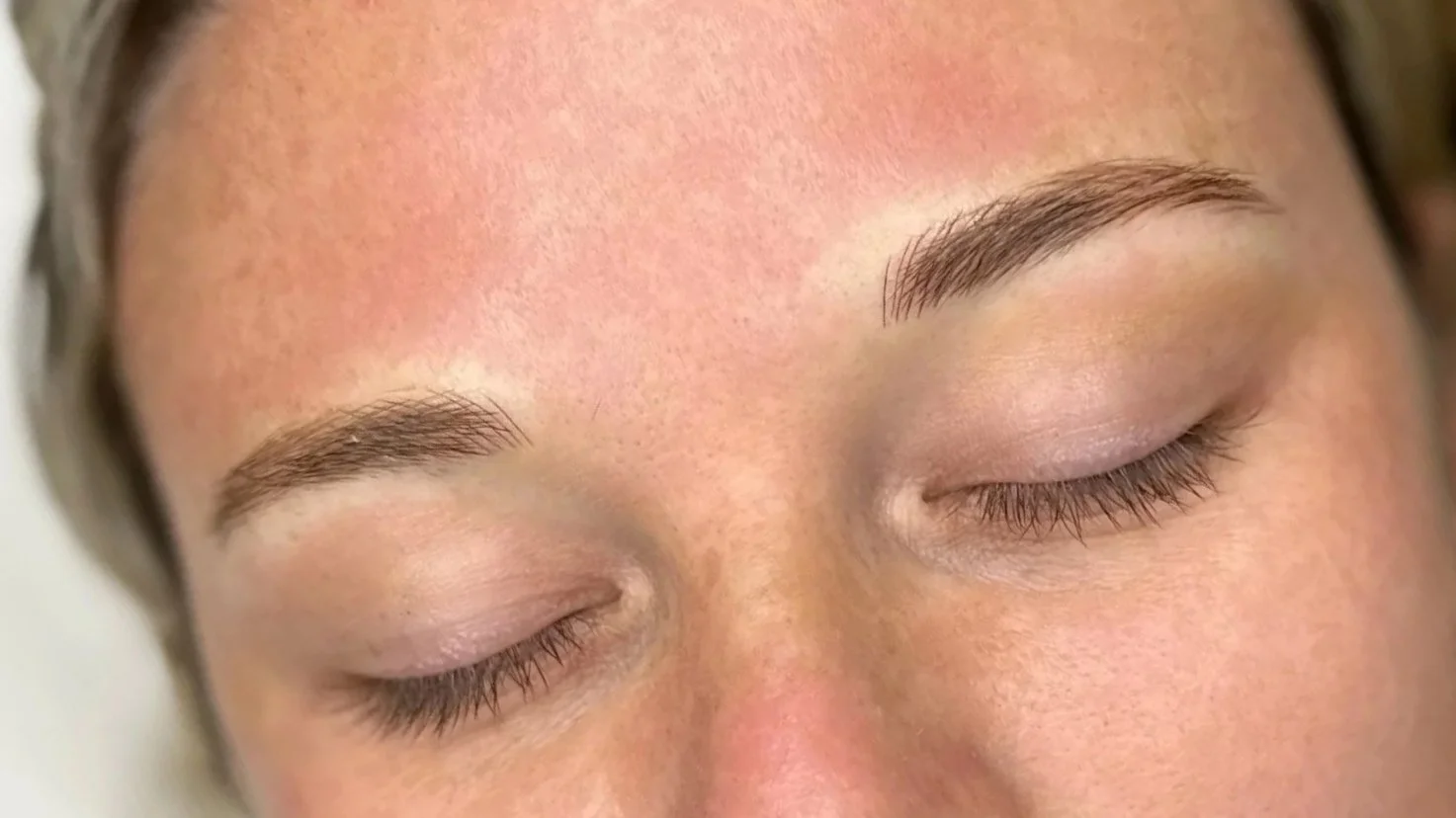Close-up of a person's face with eyes closed, showing well-groomed eyebrows and clear skin.