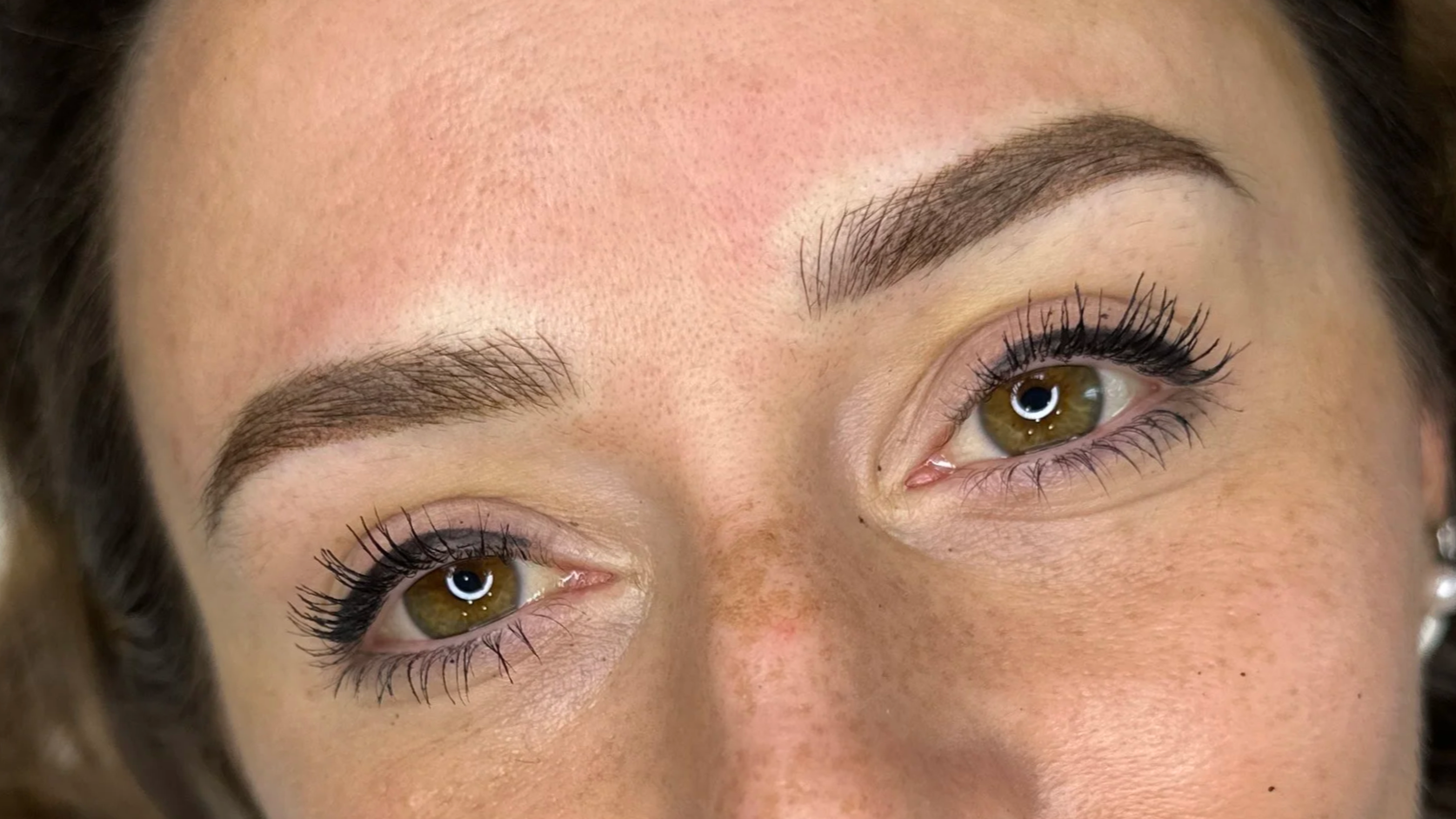 Close-up of a woman's face focusing on her brown eyes, well-groomed eyebrows, and long lashes.