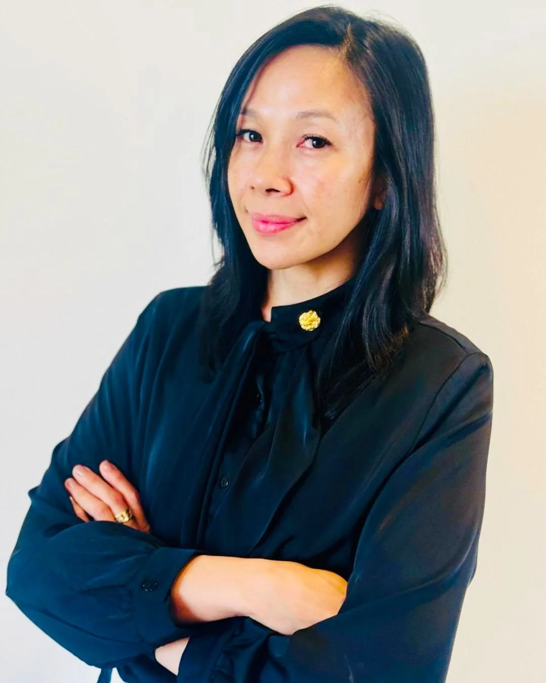 A woman with glasses, shoulder-length hair, and a white blouse sitting at a table, smiling at the camera.