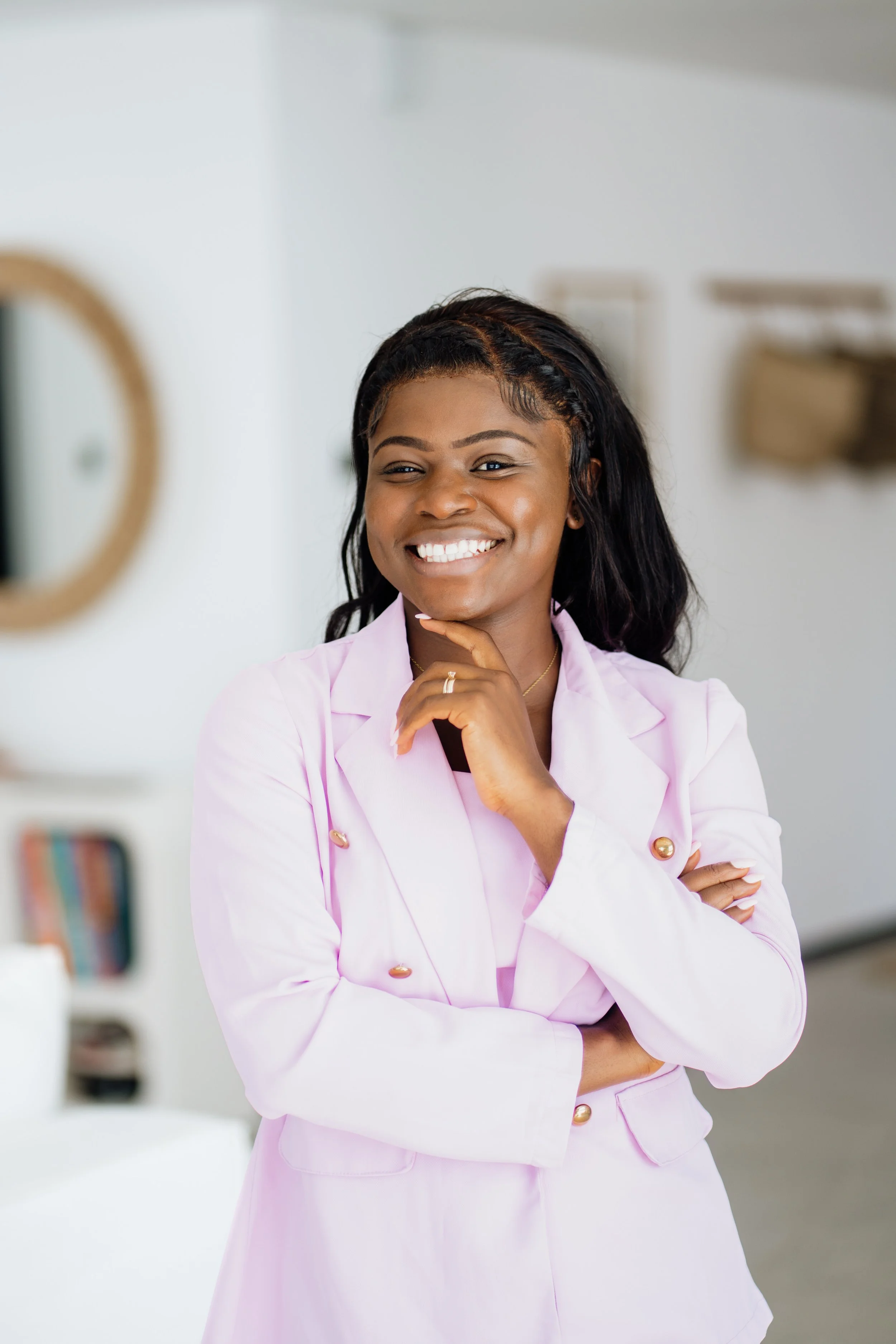 A woman in a pink blazer smiling confidentally, standing in a bright, modern interior space.