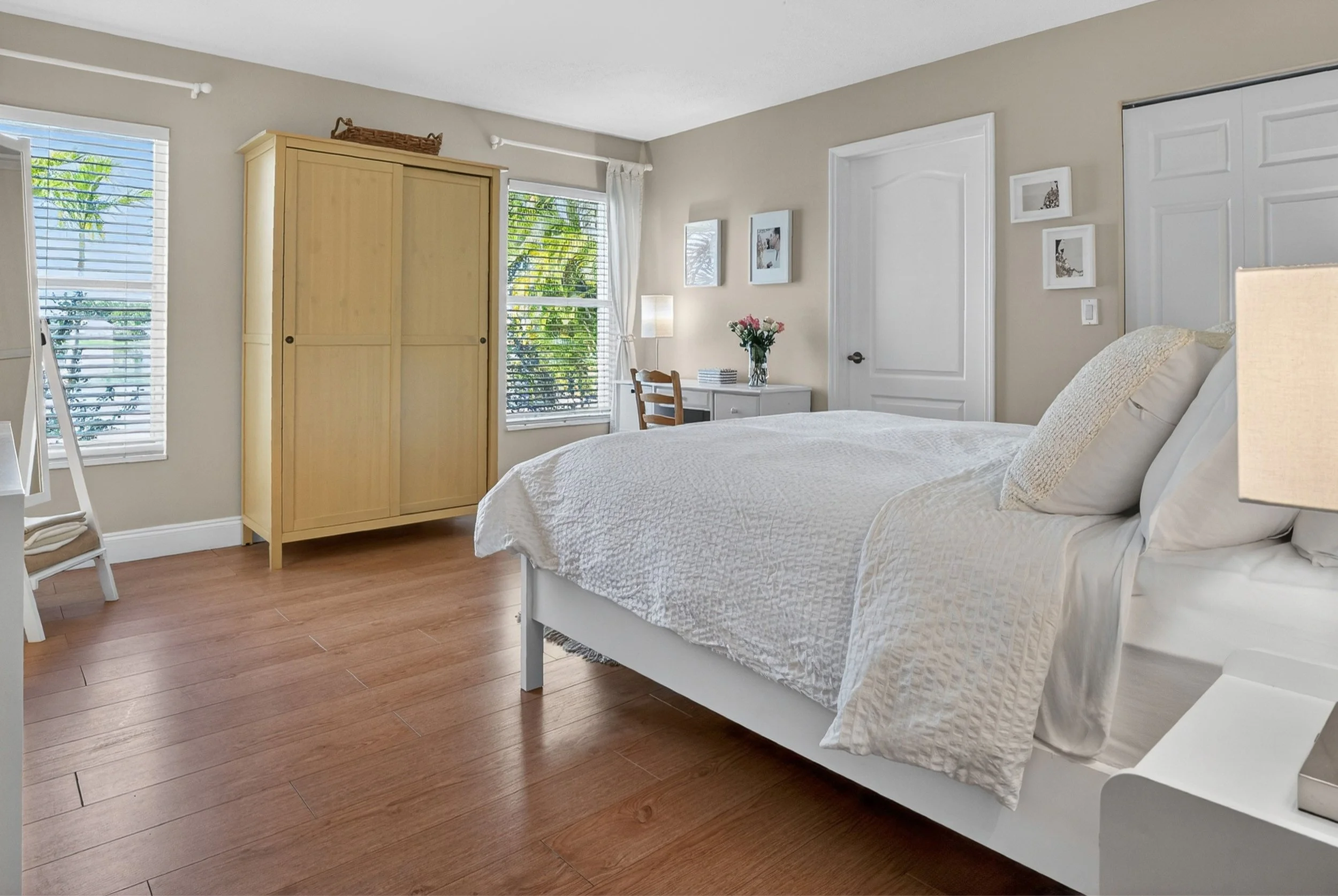 Bright bedroom with hardwood floors, soft neutral décor, and natural light creating a calm, comfortable atmosphere. A simple, airy layout and warm tones enhance the relaxing feel of the space.